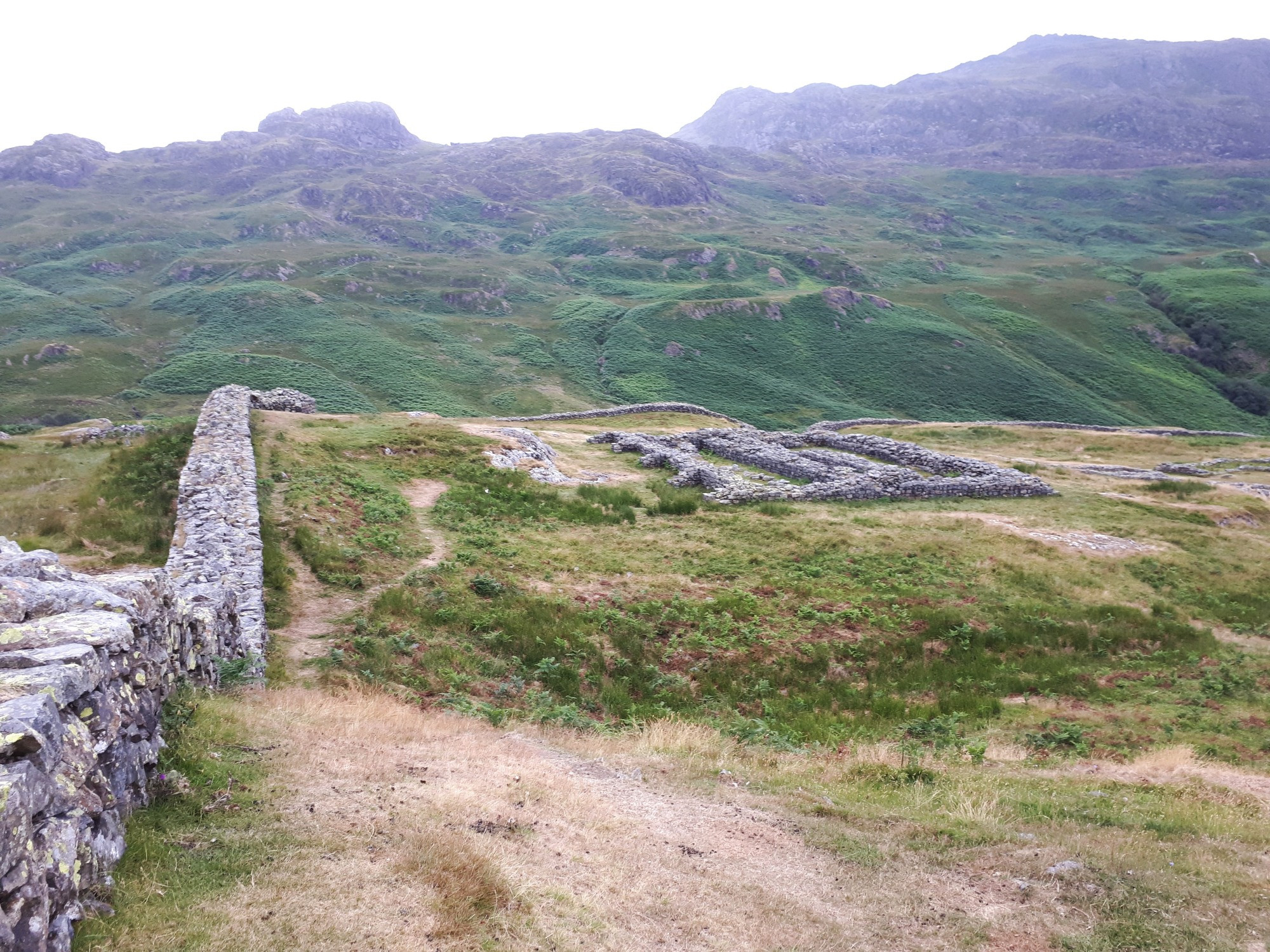 Roman ruins in a rocky scrubland field, with a misty rugged hill in the background