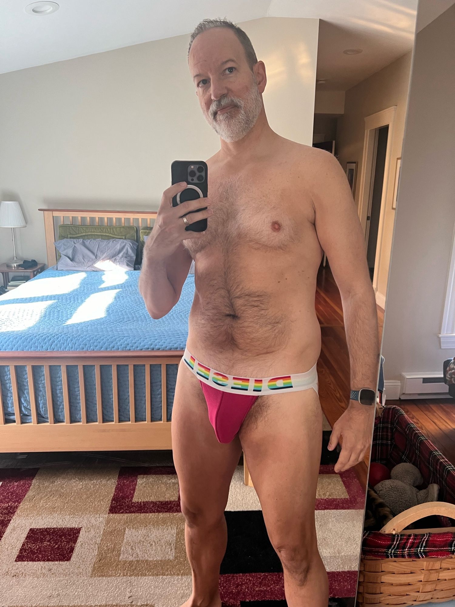 Man stands looking into a mirror to take a selfie and he’s wearing a pink jockstrap