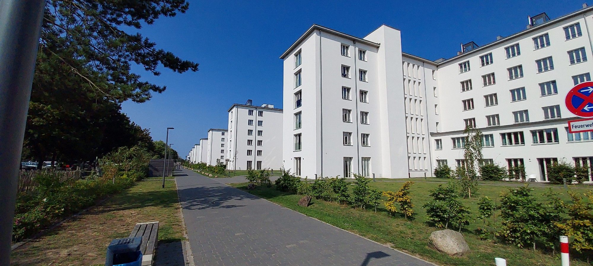 Diepblauwe hemel, links bomen en rechts een lange, lange rij van witte, afgebouwde flatgebouwen, die nu dienst doen als vakantieverblijven, woningen, horecagelegenheden.