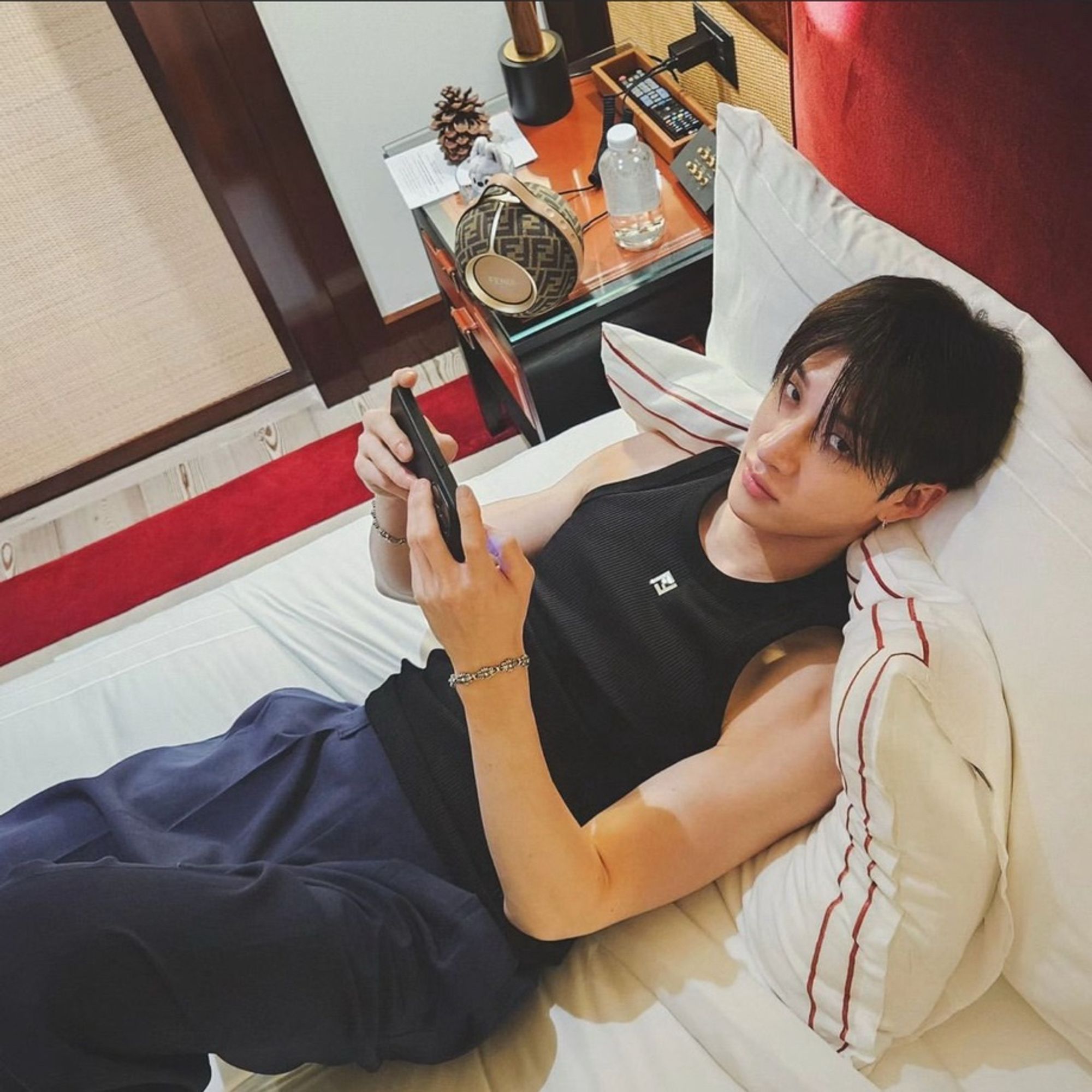 Chan laying on the bed, he’s using his phone