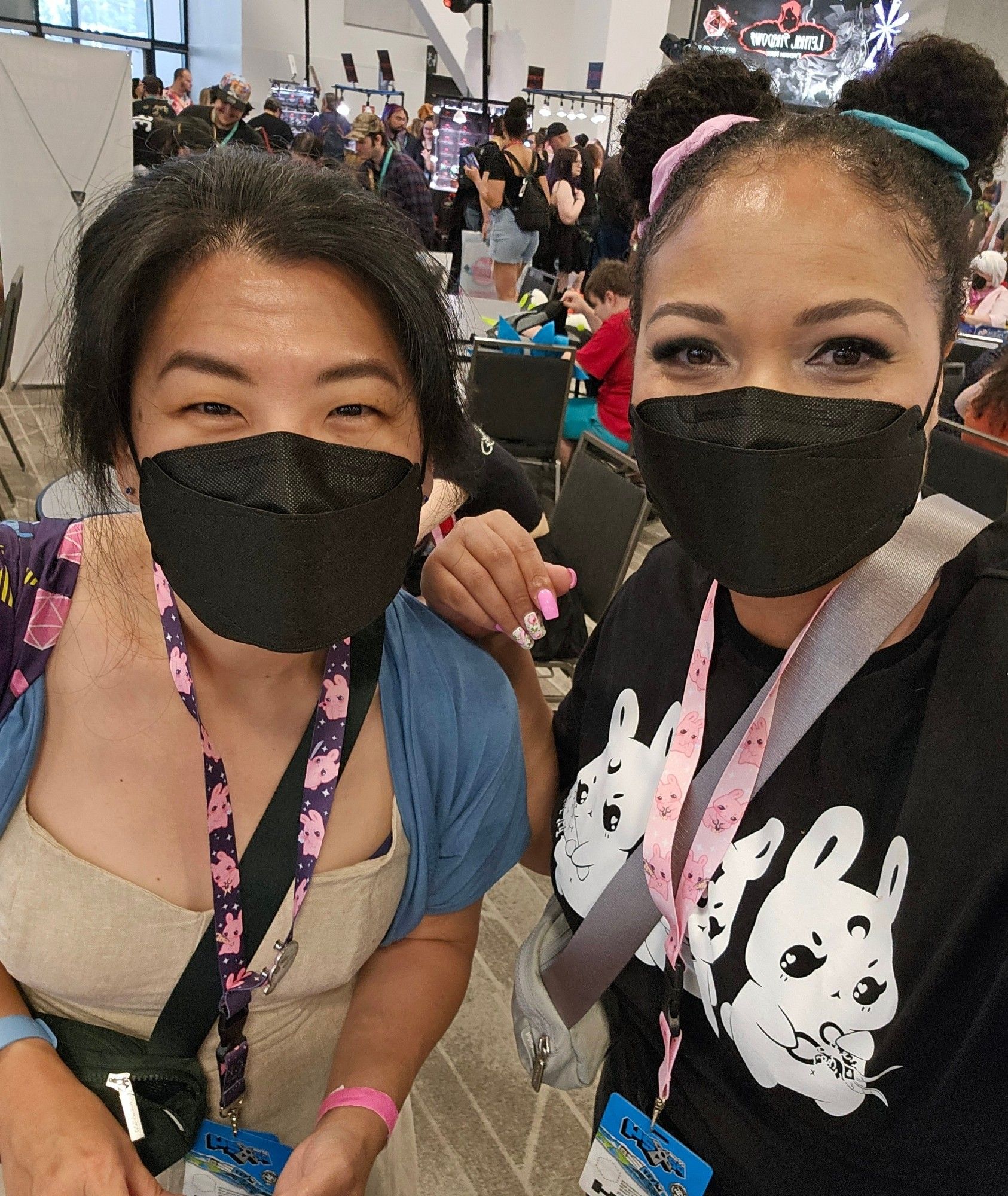 Me on the right with two buns in my hair and wearing a black face mask. Suzanne on the left wearing a black mask. People in the background in the hall.