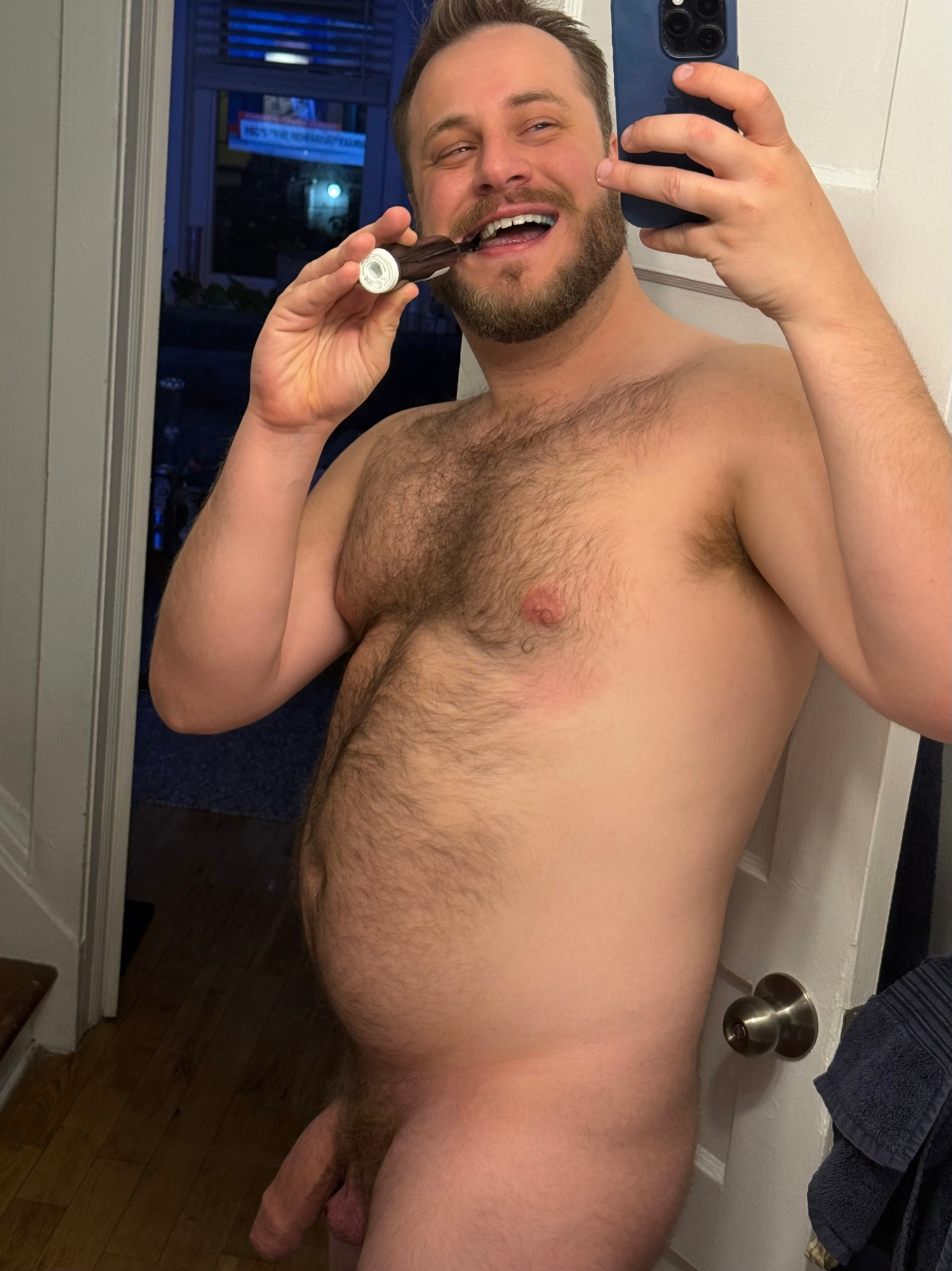 Mirror selfie of me naked and smiling while brushing my teeth. My cock is hanging very heavy and thick because I was just hard before taking the pic