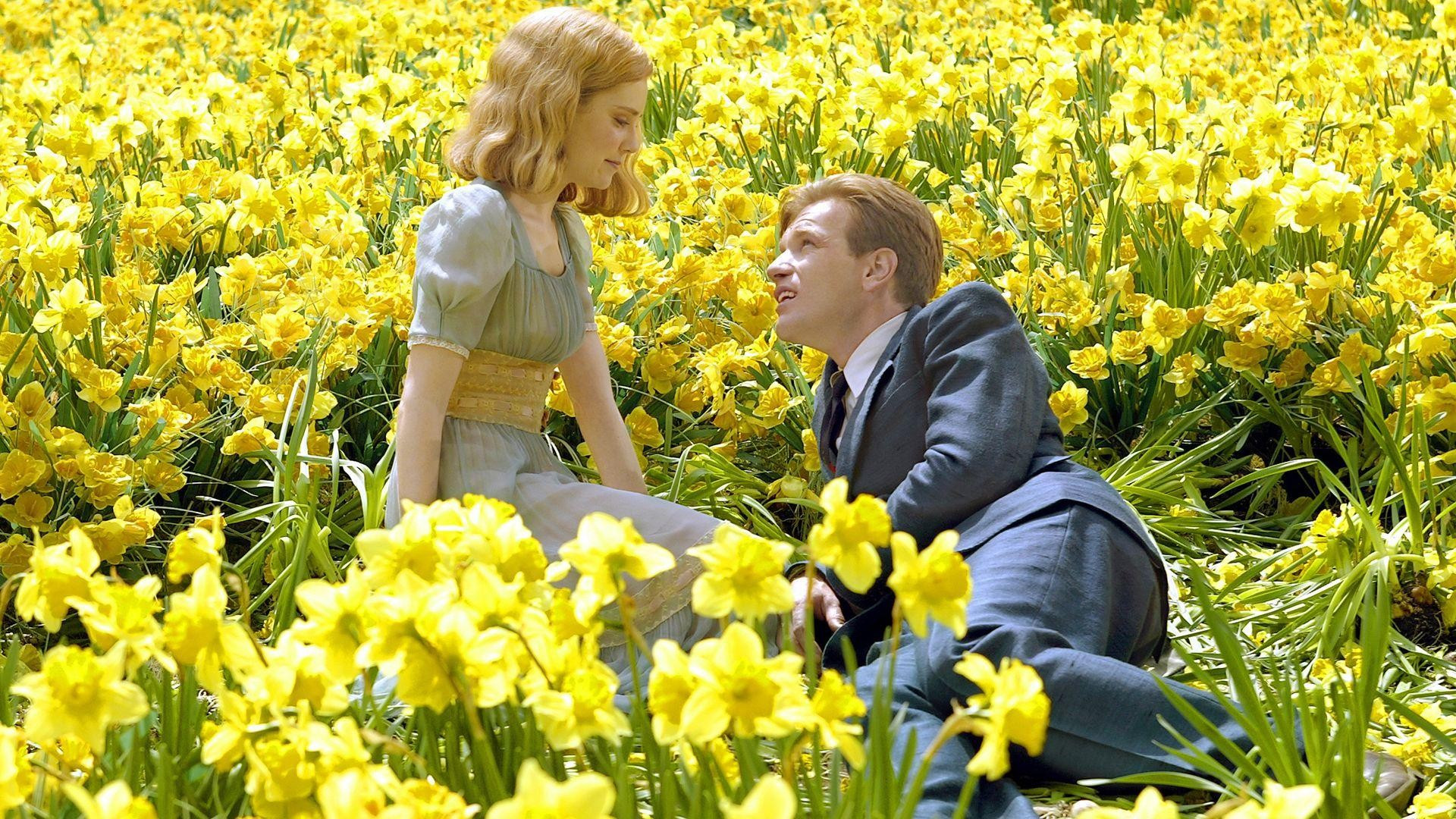 A still from Big Fish in which the two leads lie together, nicely dressed in Sunday clothes, in a bed of yellow flowers. He gazes up at her from the ground, leaning on a shoulder, while she sits above him, looking down.