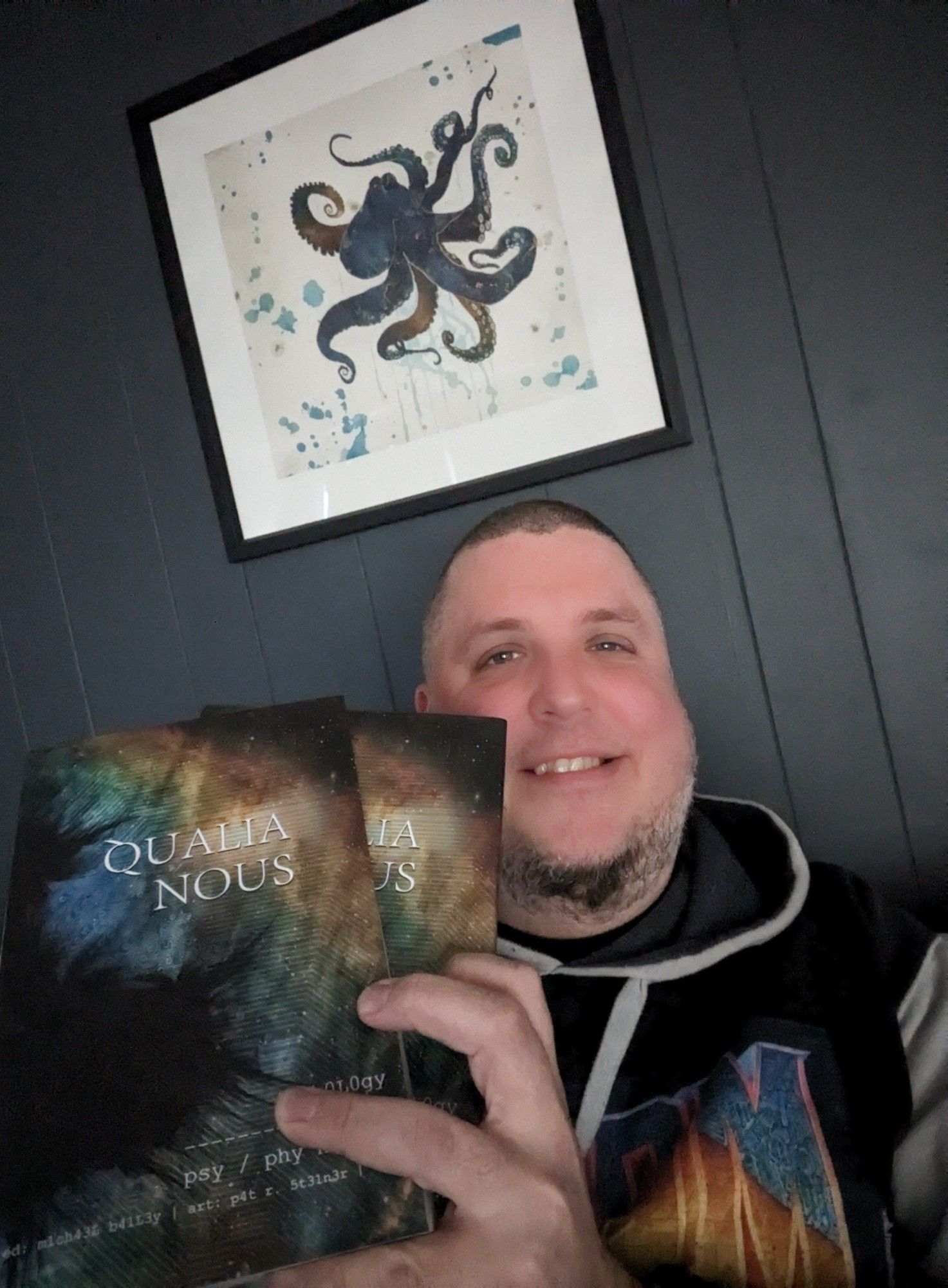 Horror author Michael J. Riser holding up the paperback and hardcover editions of the Qualia Nous 2 sci-fi horror anthology, in which his short story "Lucid Interval" appears.