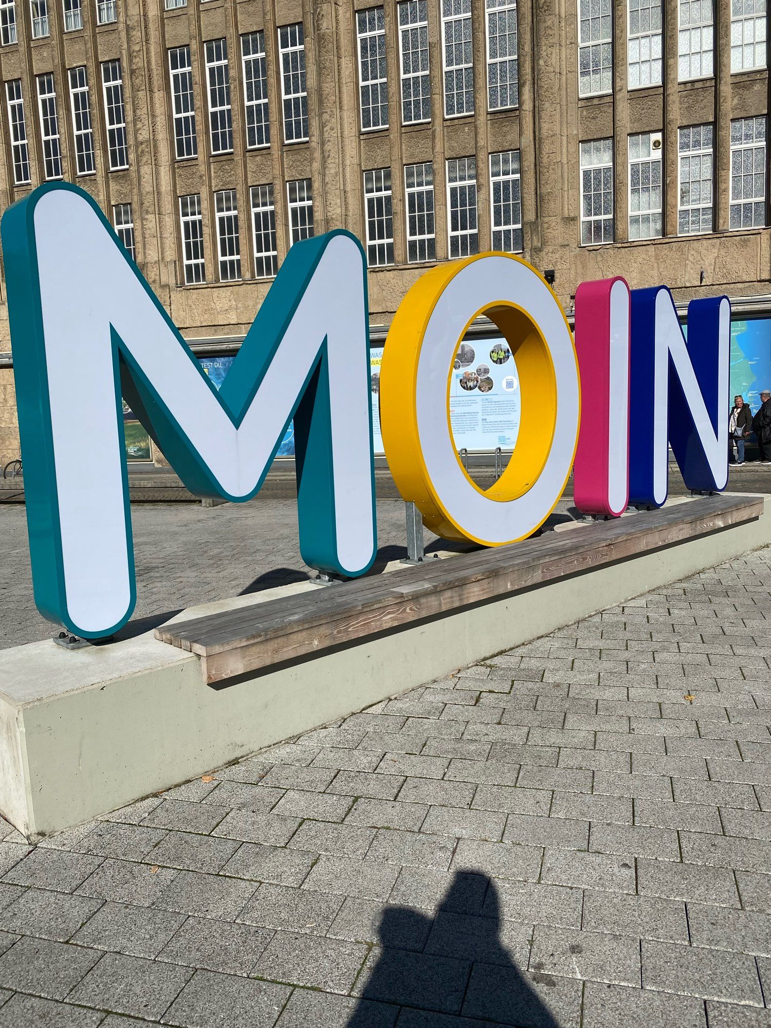 Das Wort „Moin“ als Kunstwerk in großen bunten einzelnen Buchstaben vor einem alten ehemaligen Kaufhaus