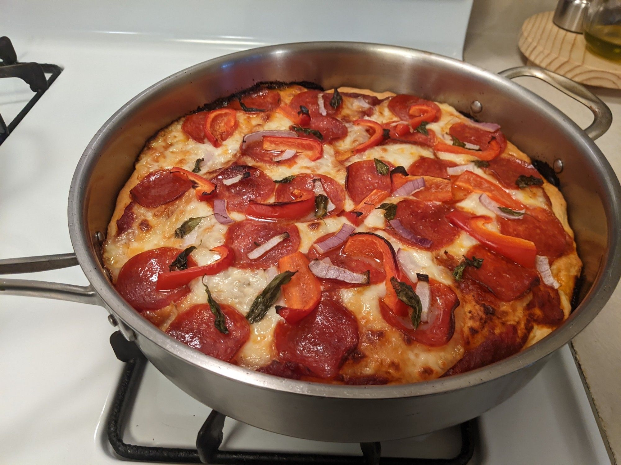 A pan pizza still in the cast iron pan. It's topped with pepperoni, mozzarella, red onion, red bell pepper, and fresh basil leaves.