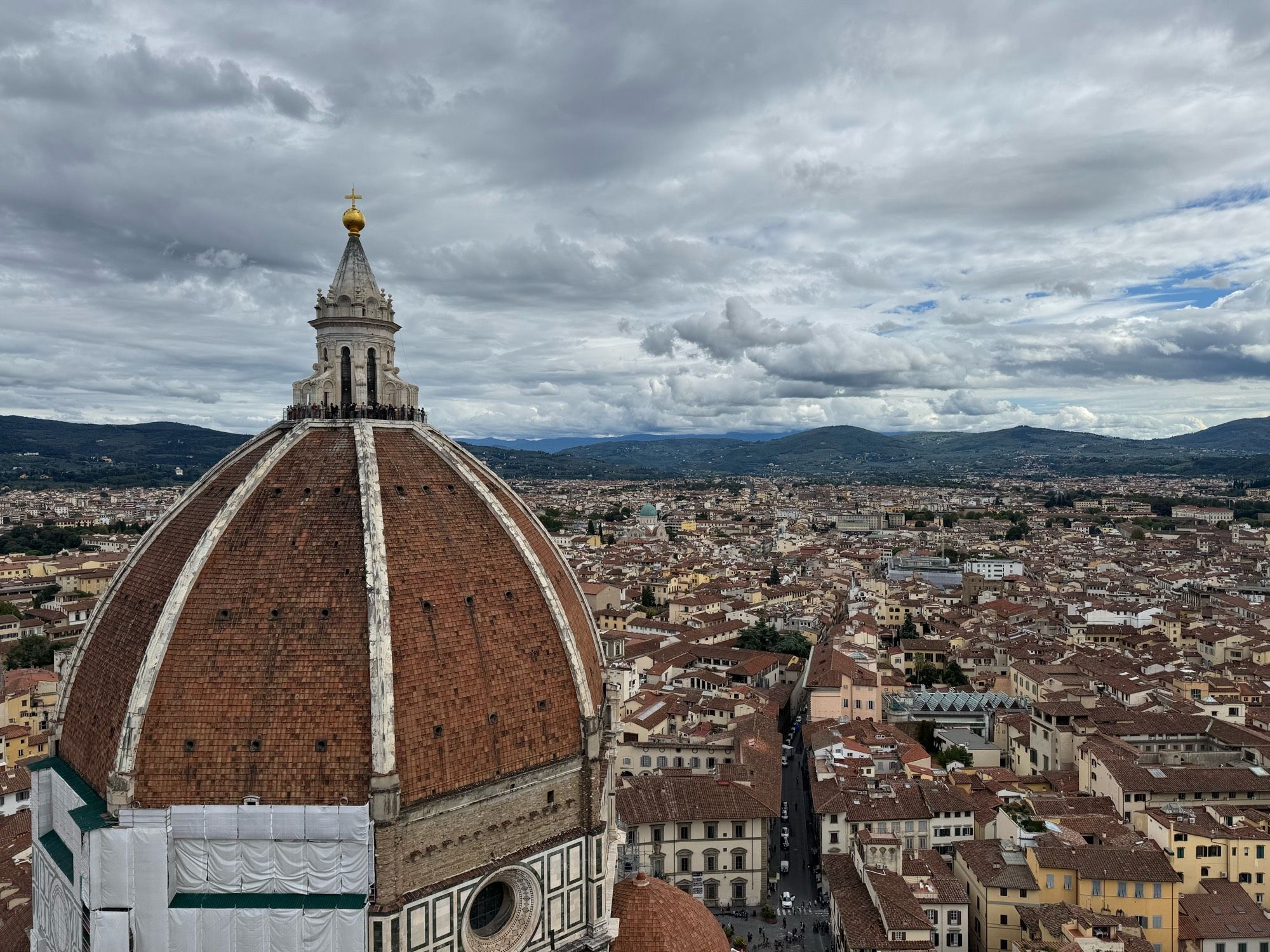 A photo taken atop the bell tower besides the grand cathedral of Florence. The enormous dome takes up about a third of the entire picture of the skyline. Thick clouds cover the sky, but let enough light through to brighten the whole picture