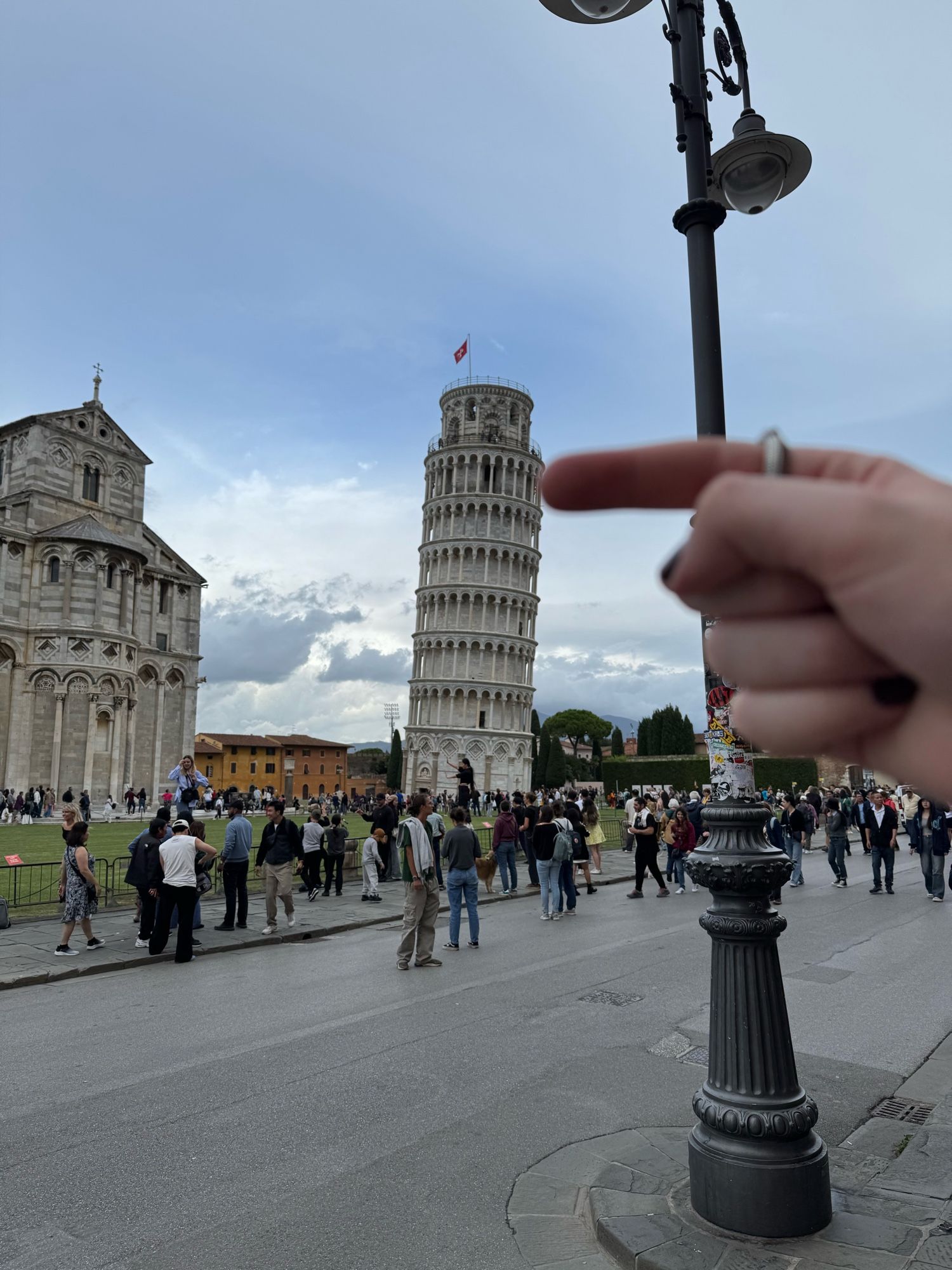 A photo of me seemingly pushing the leaning tower of Pisa back towards an upright position. A large crowd of people is also visible. My finger is blurred