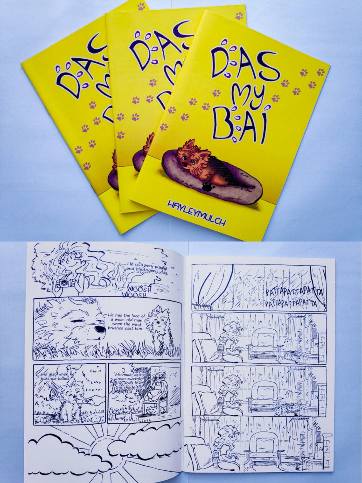 Three copies of the comic Das My Bai. It's a mostly yellow book cover with a dog in a bed and the title of the book written in big text. It also shows some interior pages of the comic where me and Jack are outside on a warm and windy day, and where we're inside on a rainy day.