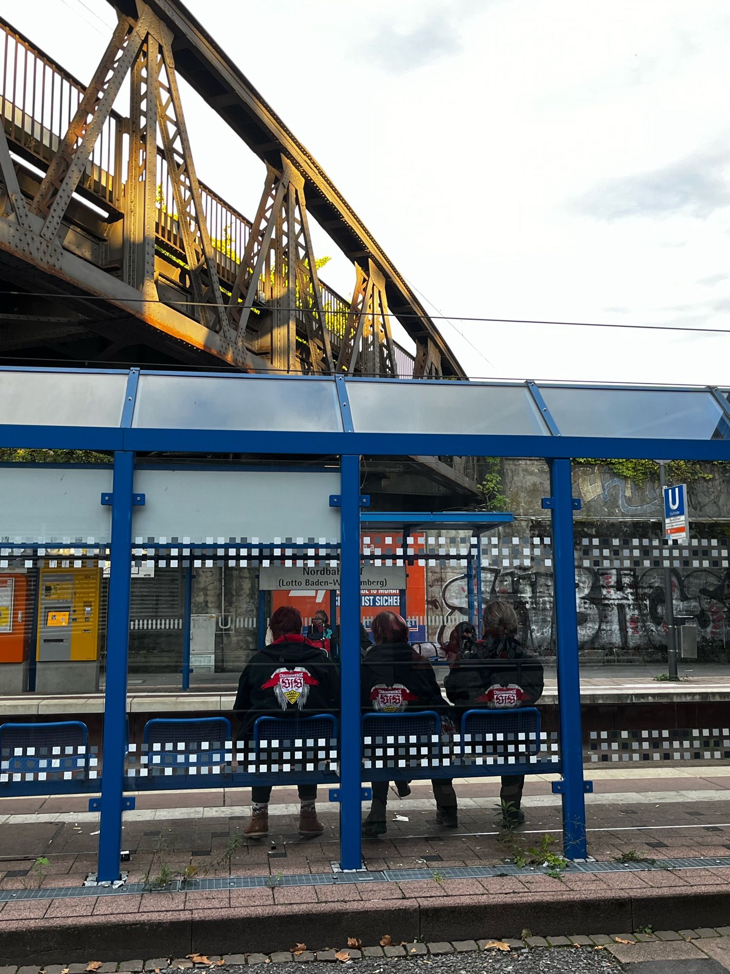 Drei VfB Stuttgart-Fans sitzen im Wartehäuschen an der Stadtbahnhaltestelle Nordbahnhof