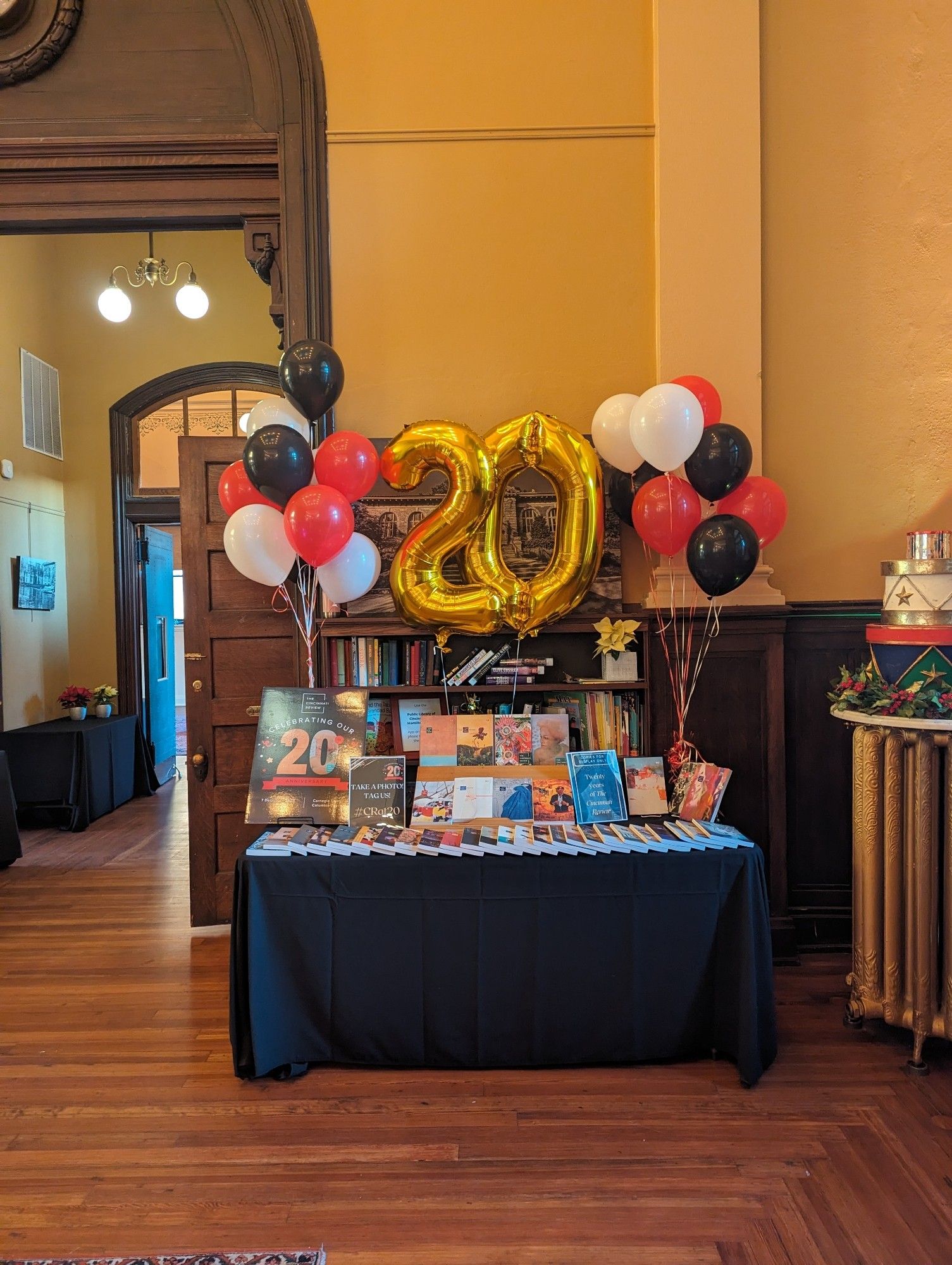 A table with 40 magazines stacked on it, plus red, black, and white balloons and gold balloons that spell out twenty