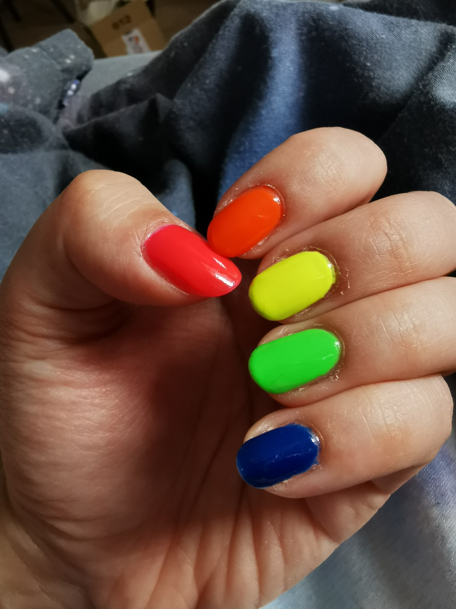 Ein Bild von meiner linken Hand. Alle fünf Finger sind in verschiedenen Neonfarben lackiert:
Daumen - neonpink
Zeigefinger - neonorange
Mittelfinger - neongelb
Ringfinger - neongrün
Kleiner Finger - neonblau (dunkel)