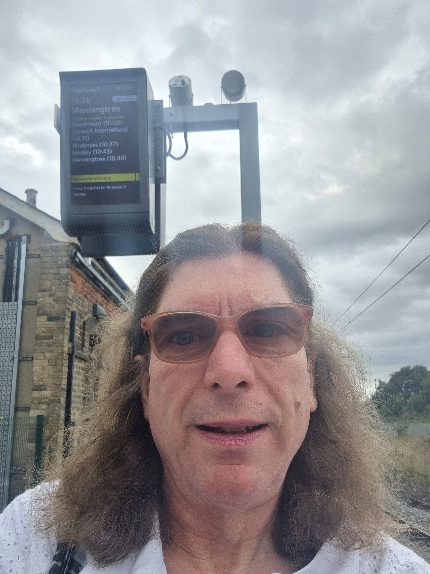 Me on a railway platform with a train indicator screen behind me.