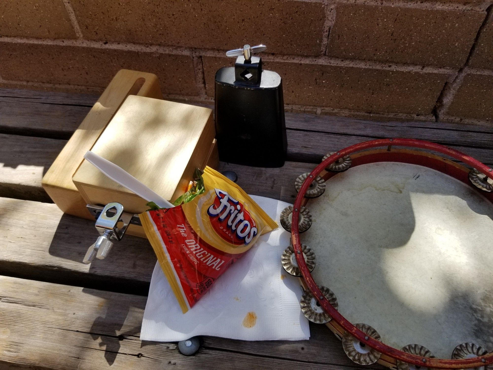 Two woodblocks, cowbell, a janky looking tambourine, and a Fritos bag with a fork sticking out containing beef red chile, cheese, lettuce onion on the Fritos.