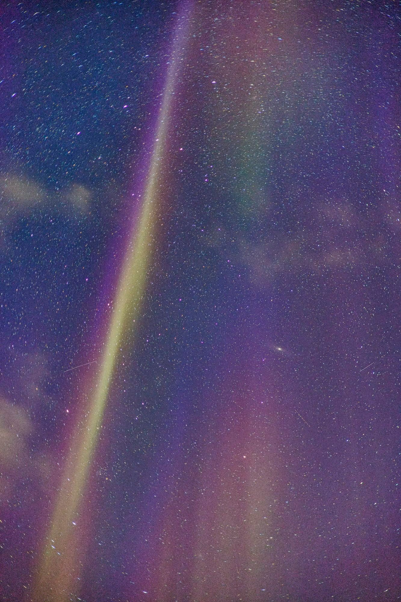 A view straight up at a star-filled sky, with yellow, pink and green aurora