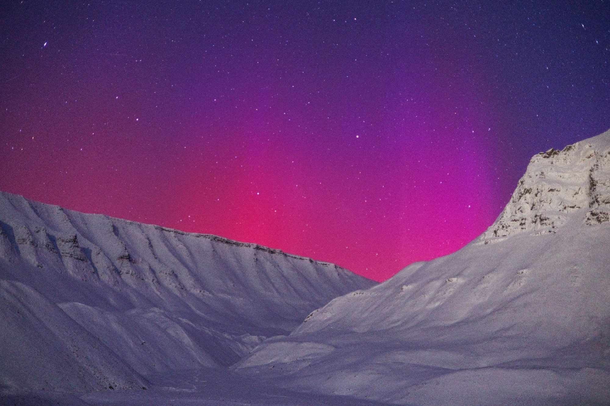 Hot pink and purple aurora over a snowy mountain