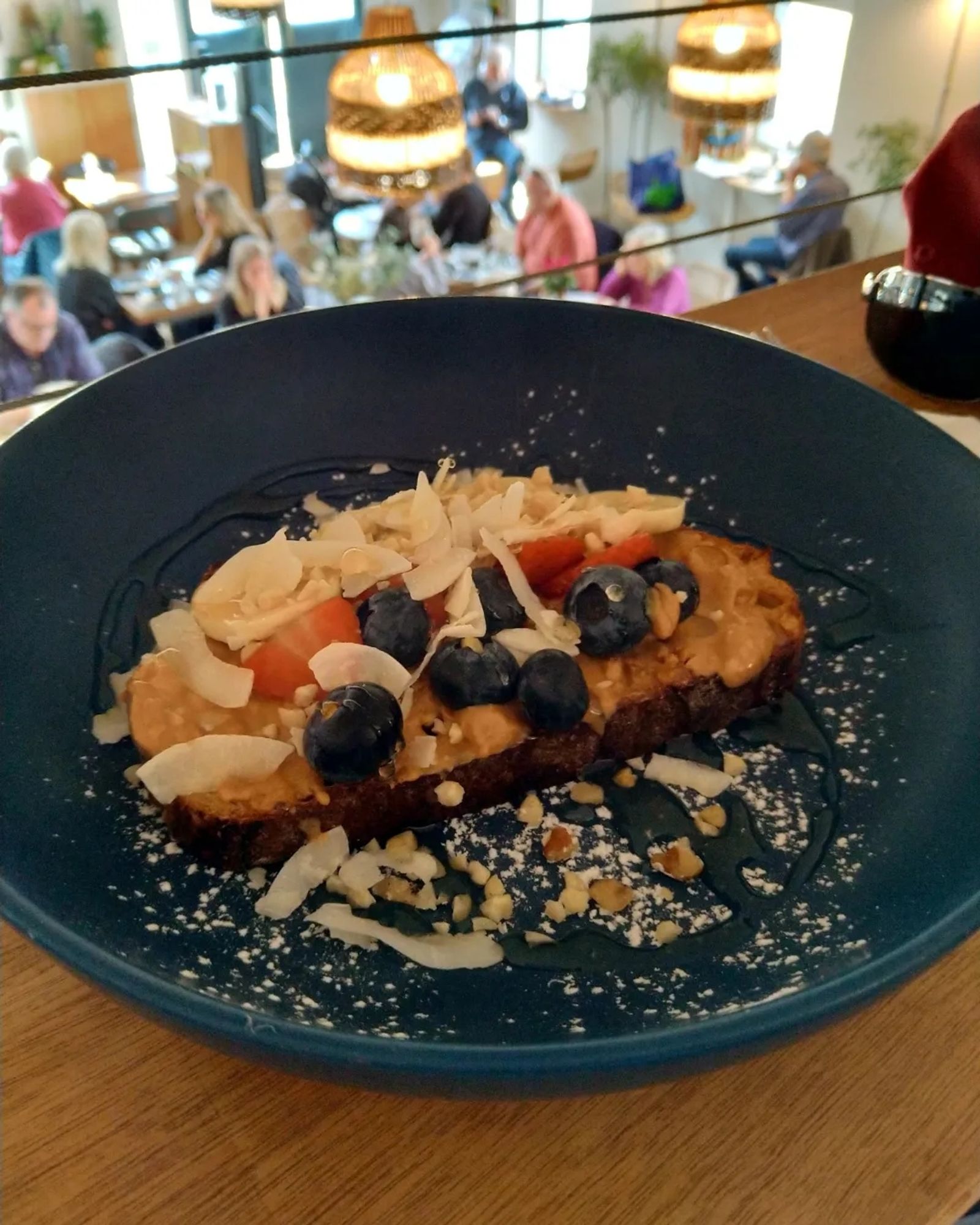 Peanut butter on toast covered with strawberries, blueberries, banana and coconut in a dark blue bowl