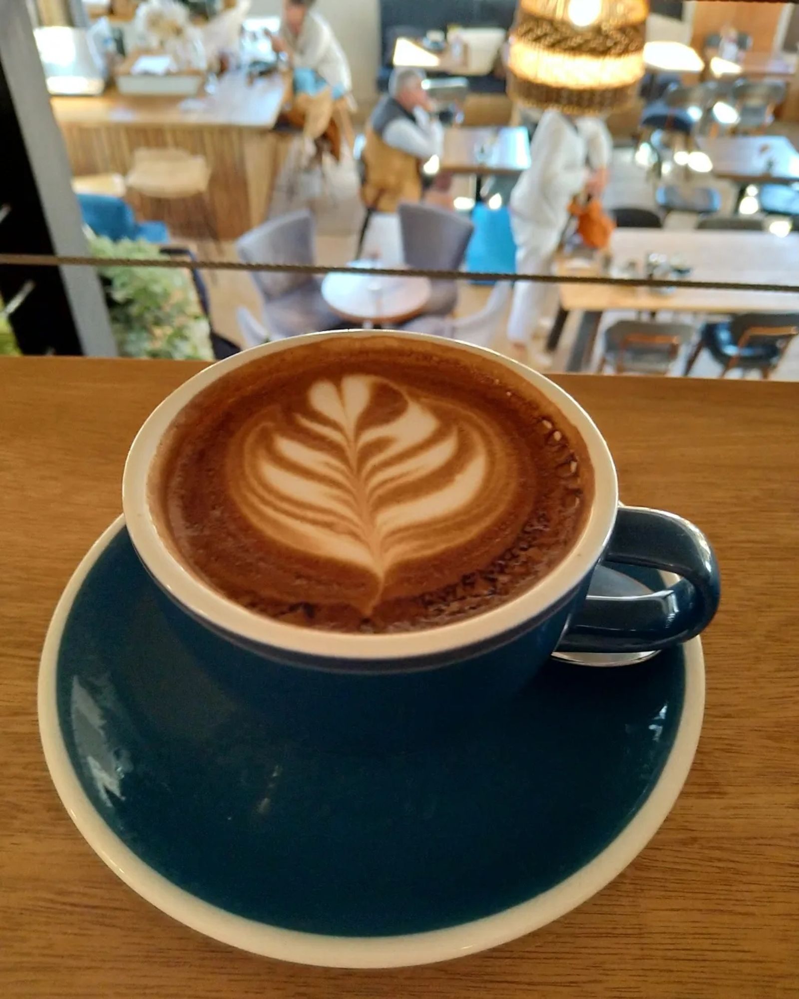 Flat white coffee in a cup and saucer overlooking a coffee shop