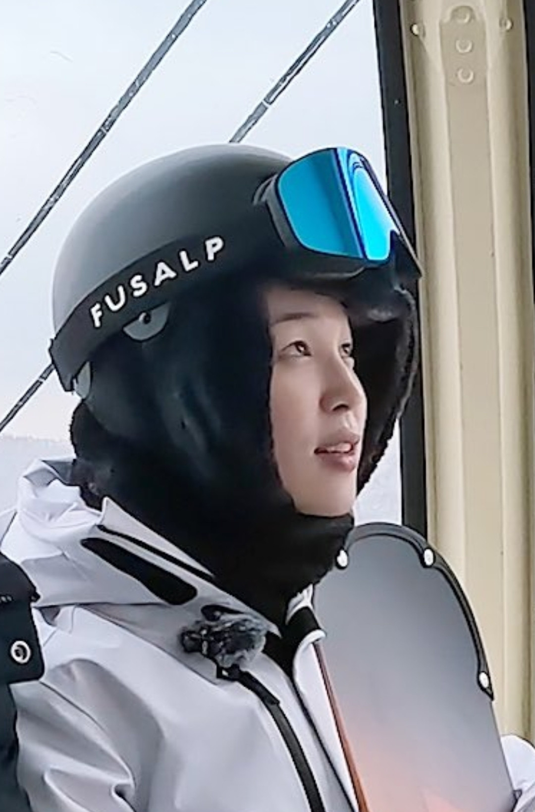 Jimin wearing a big ski cask with goggles ln the cask