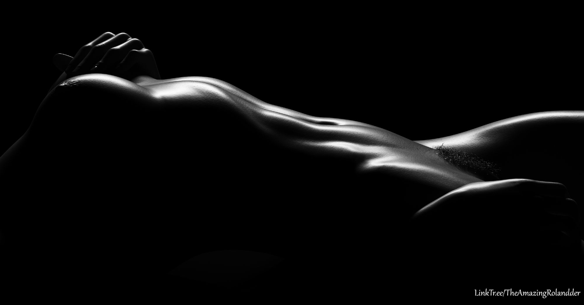 Black and white high contrast image of a nude woman, lit so only her chest to legs are lit, angled so barely anything is visible.