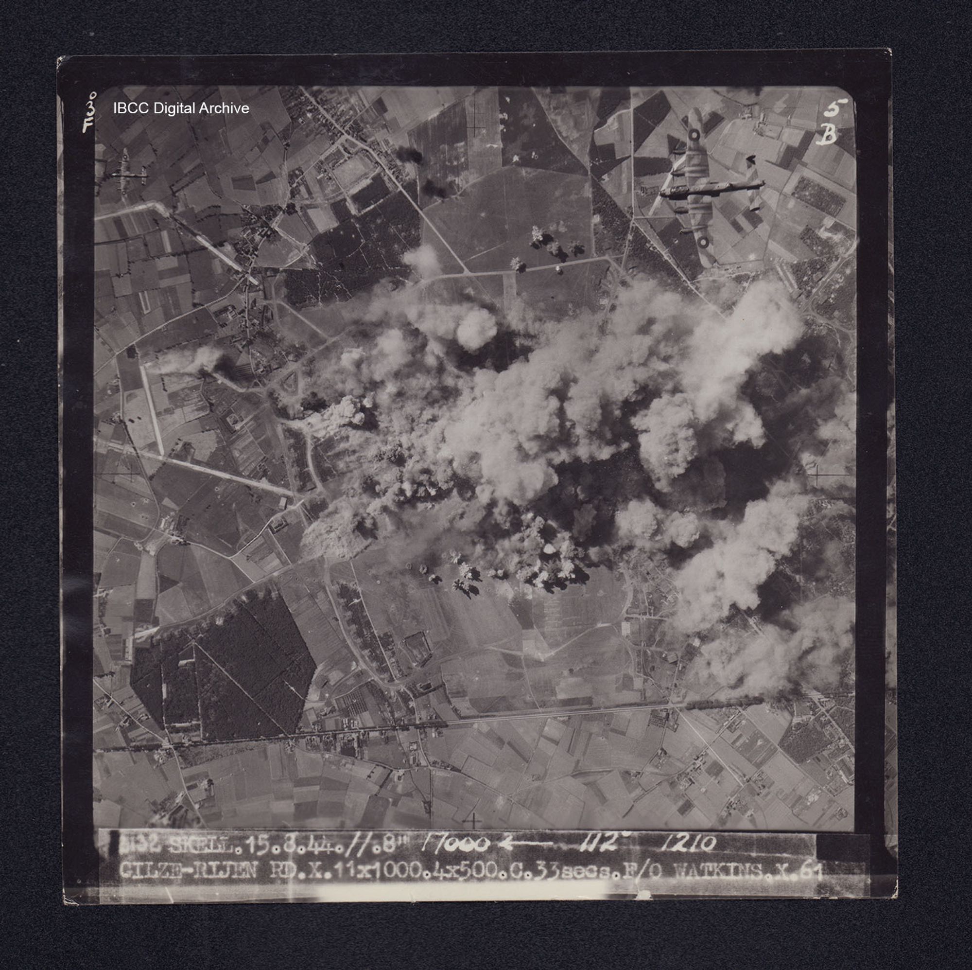 Target photograph of Gilze-Rijen. Partially obscured by smoke and dust, bomb explosions visible. The end of the runway, a taxi way, two Lancasters flying below and roads also visible. Captioned '3°F', '5B', '2132 SKELL.15.8.44.//.8" 17000 [arrow] 112° 1210 GILZE-RIJEN RX.X.11X1000.4X500.C.33secs.F/O WATKINS.X.61'. On the reverse 'F/O WATKINS GILZE-RIJEN 15.8.44'. 'MH'.
IBCC Digital Archive item 7532