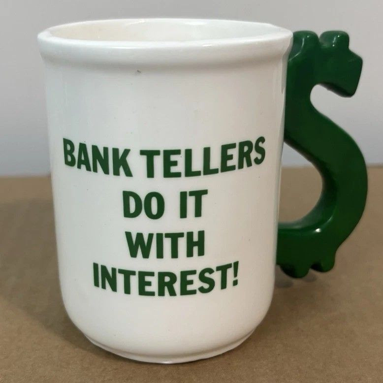 White mug with a green dollar sign handle and text reading "Bank Tellers Do It With Interest!".