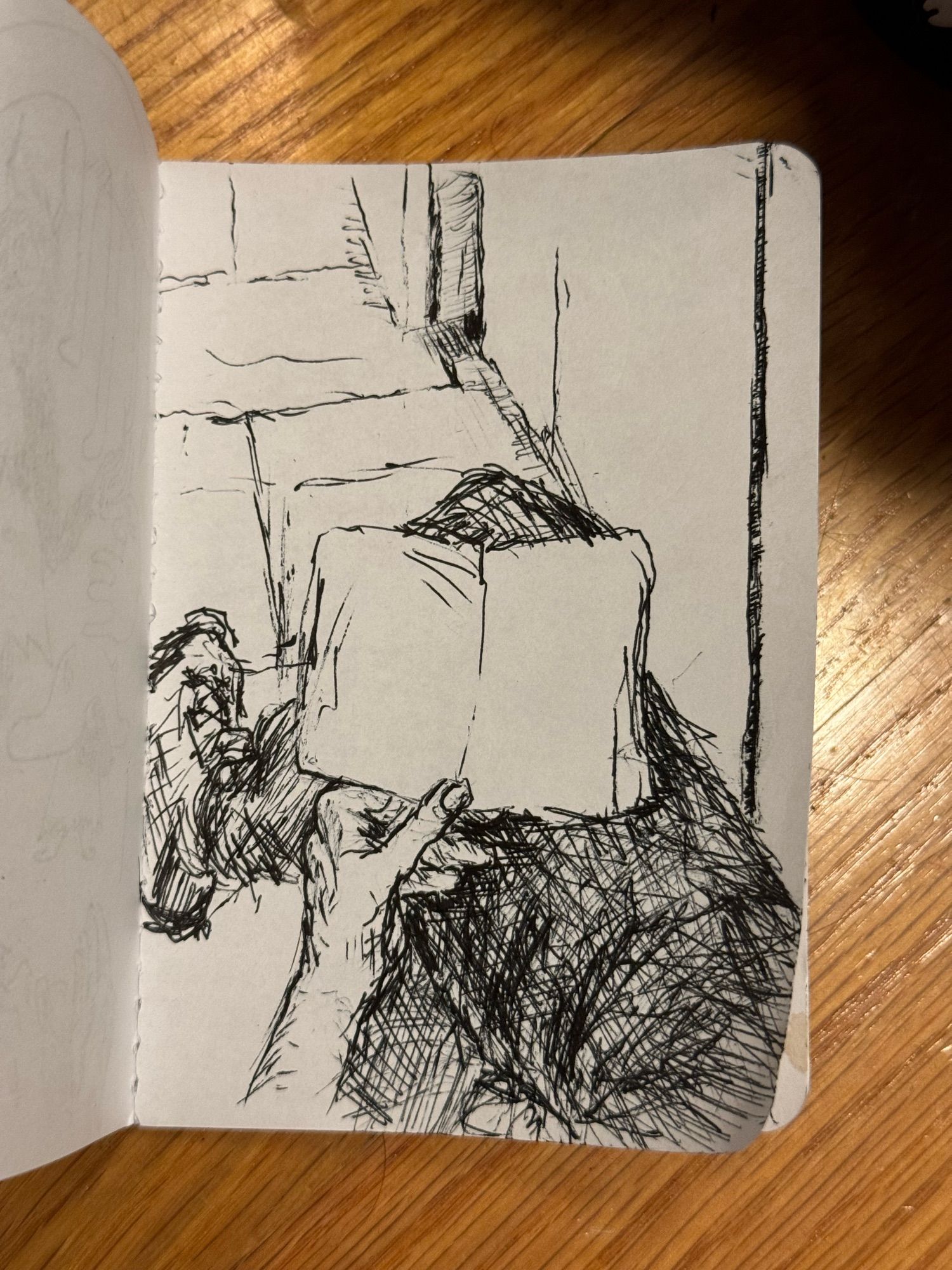 Pen drawing. My hand holding the sketchbook on my crossed legs. On my right side are cabinets and the corner of a fridge in the break room