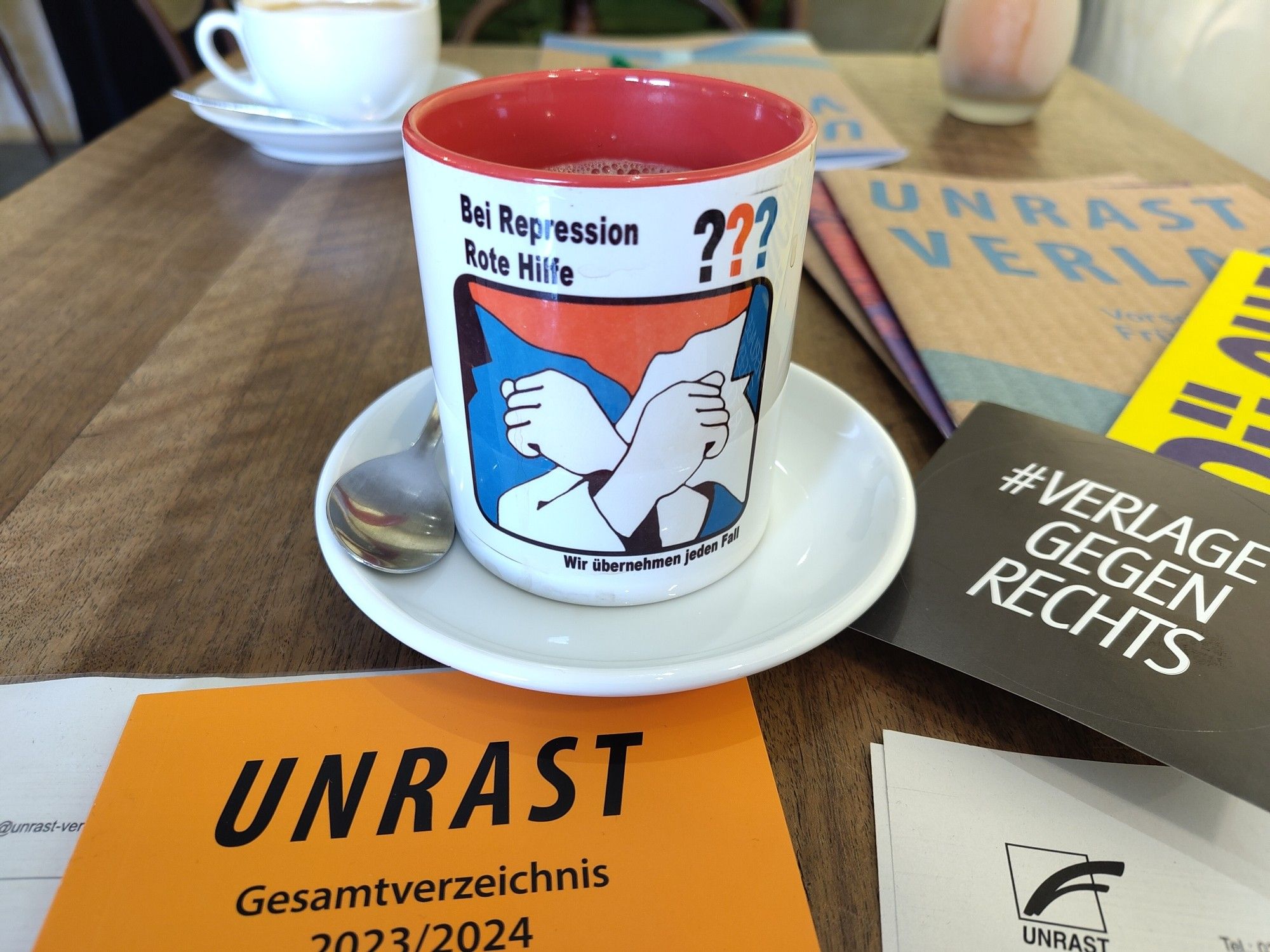 Ein Tisch mit mehreren Broschüren vom Unrast Verlag sowie Aufklebern von #VerlageGegenRechts und einer Kaffeetasse der Roten Hilfe.