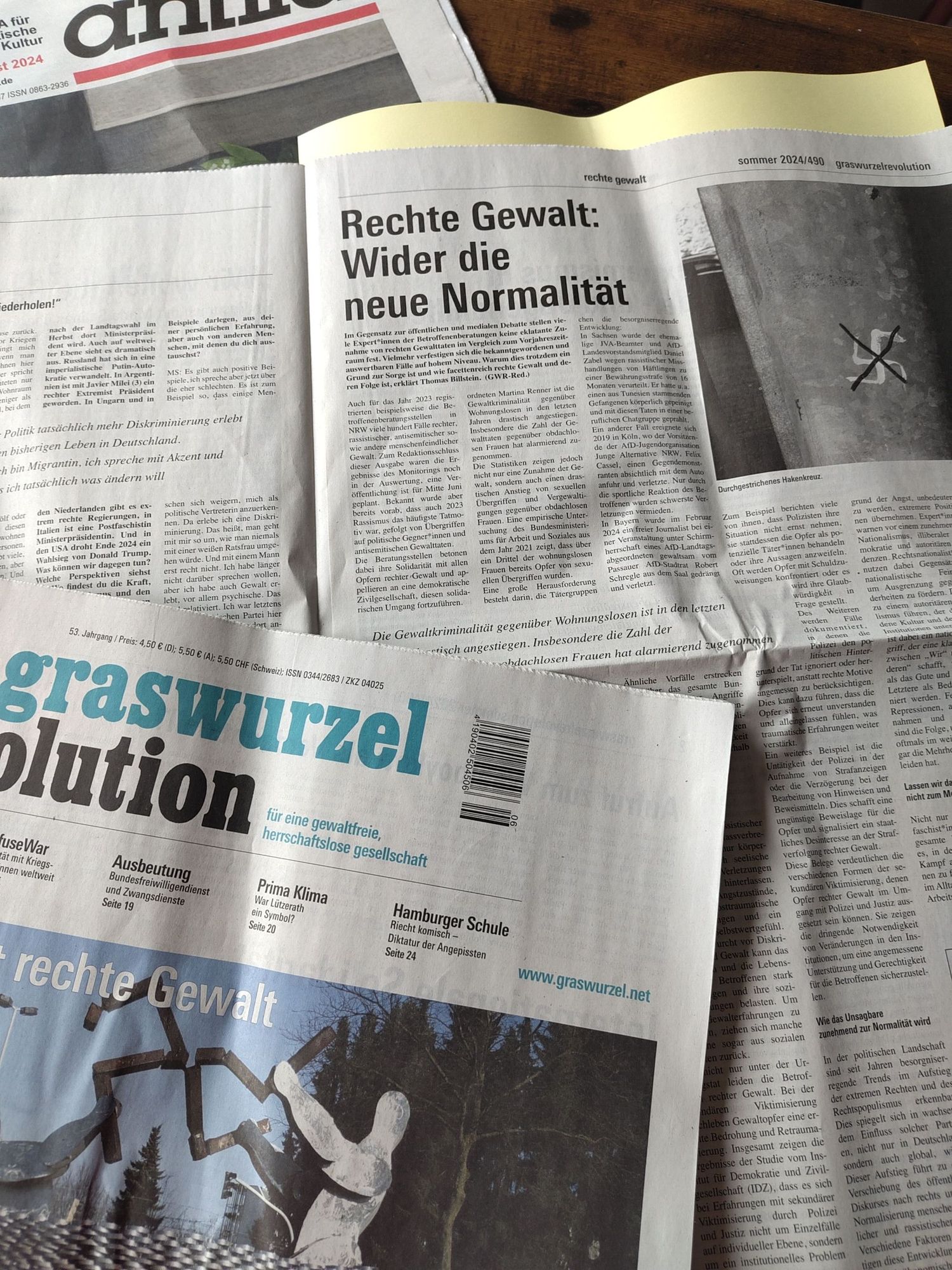 Eine aufgeschlagene und eine zugeklappte aktuelle Ausgabe der monatszeitschrift Graswurzelrevolution liegen auf einem Tisch.