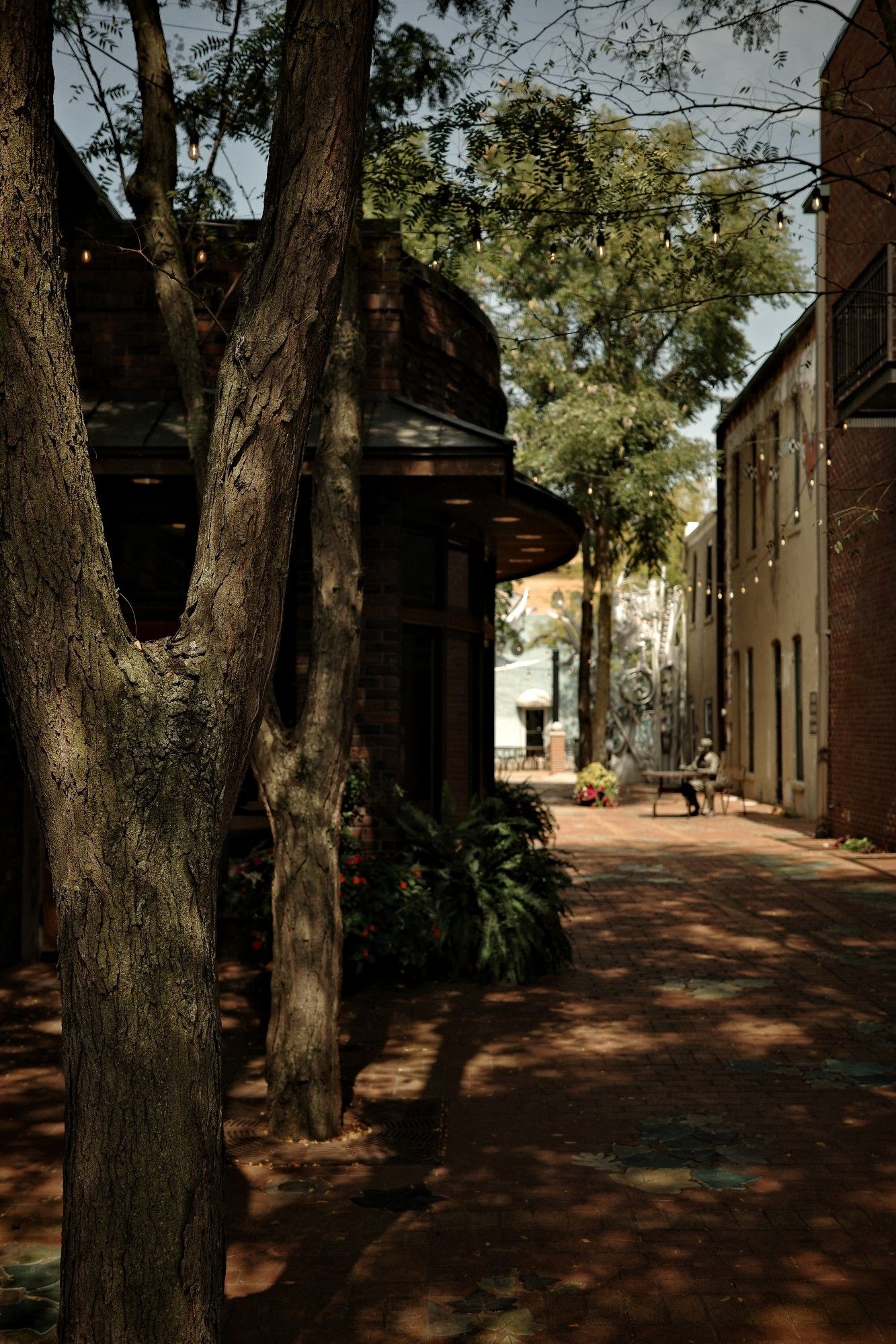 A narrow, shady courtyard with a statue of a man sitting at a table.