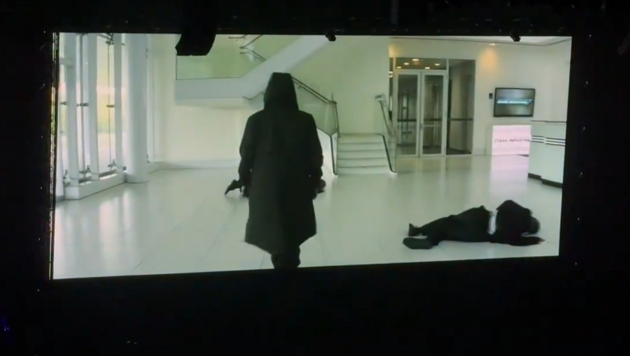 A hooded guy with a long black coat walking with people laying in the floor who happens to be MCU Sam, that's very hot of him