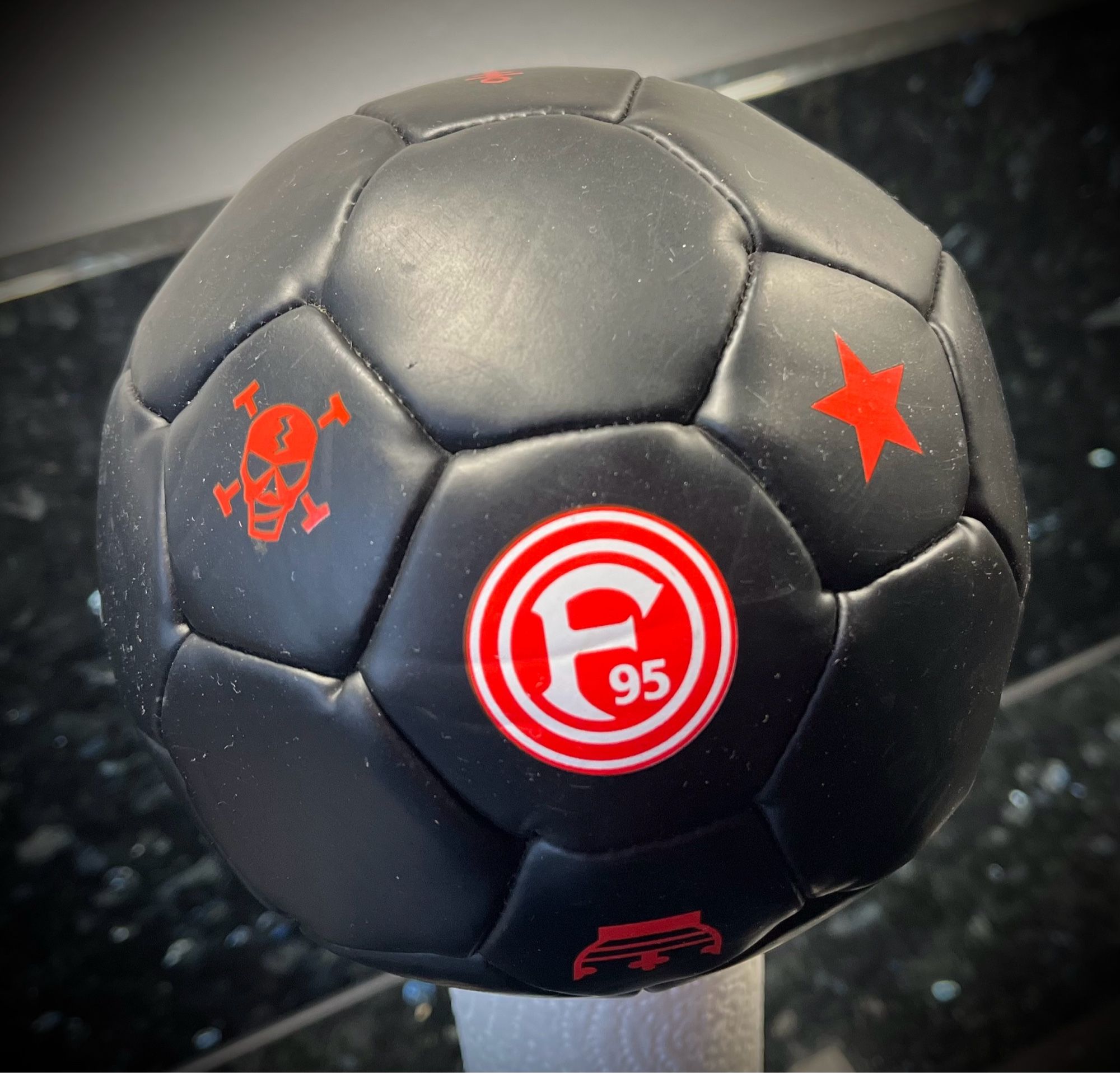 kleiner schwarzer Fussball mit F95-Logo, einem Totenkopf und einem Stern, jeweils rot