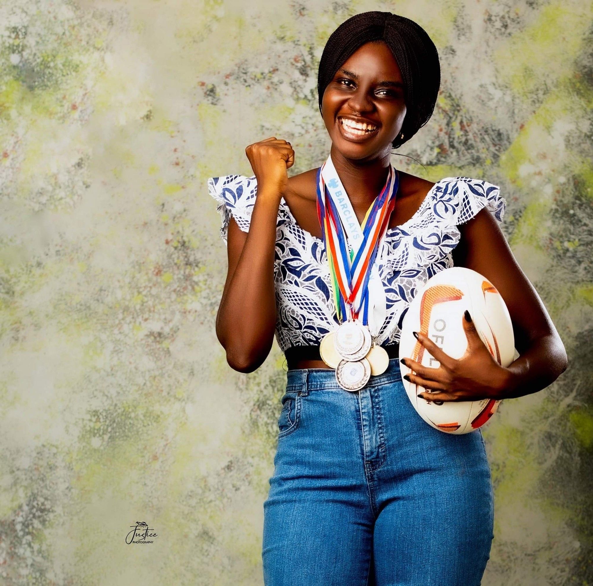 Rachel Ankomah holding a Rugby League ball and wearing her medals. She's doing a celebratory pose, and she's wearing a cool denim with a floral blouse outfit.