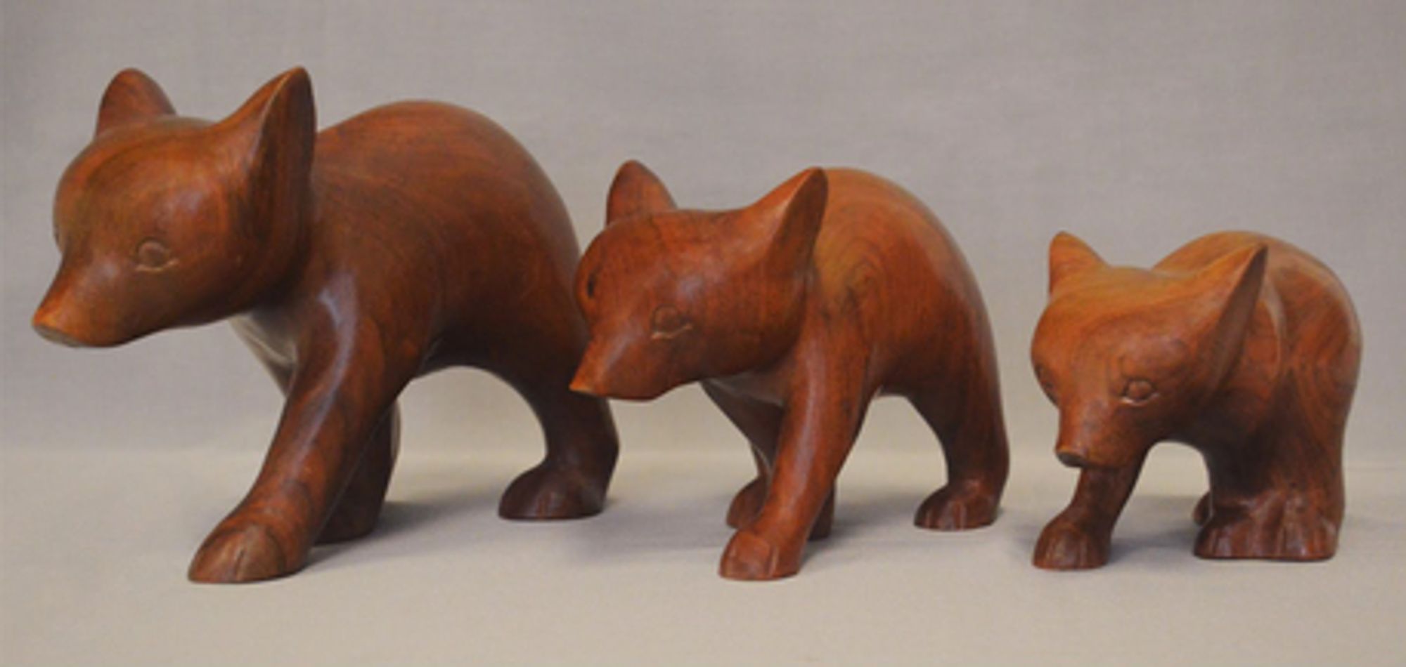 "Wooden Bears" in cherry wood, by Amanda Crowe.
A family of 3 bears, big, middle, and small, standing next to each other on four legs. The style is neat, almost minimal.