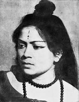 A black and white photograph of a young Bangladeshi woman, Novera Ahmed, with long hair, wearing a bindi on her forehead. She is gazing off to the side, wearing a long beaded necklace. She has a nice eyeliner cat eye look.