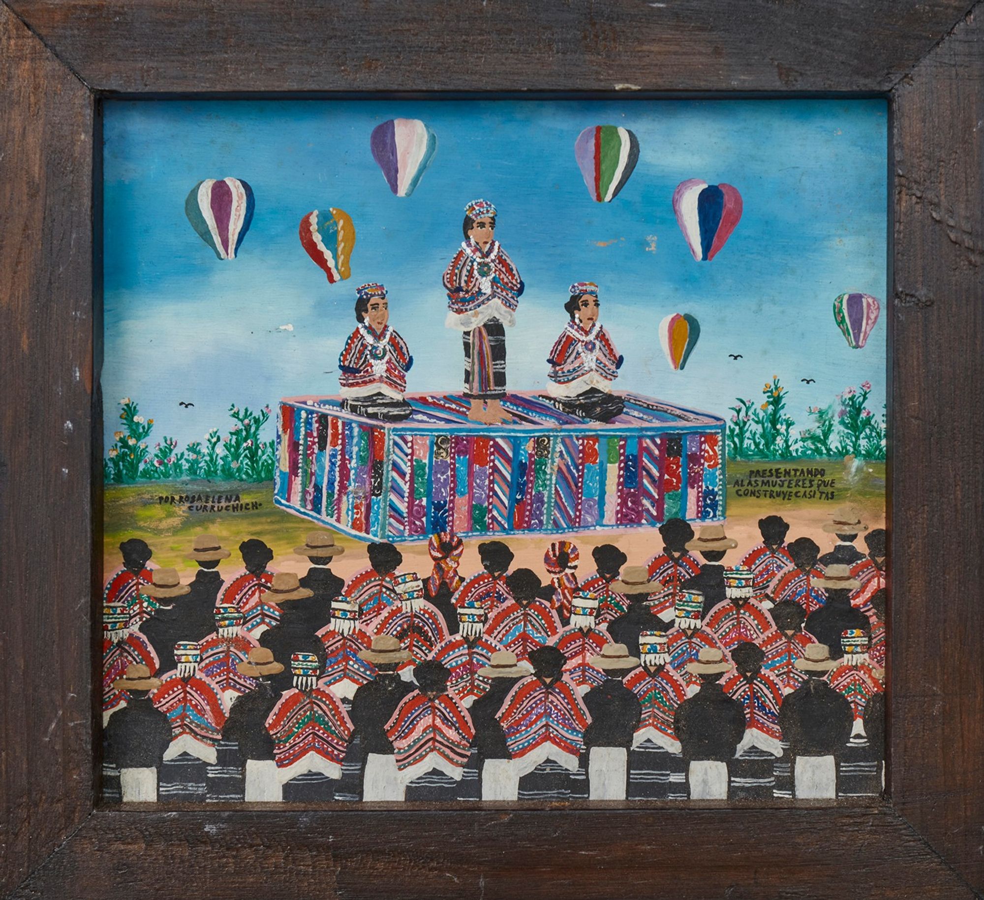 A painting showing a celebration of three Maya women seated at a podium, wearing crowns, in front of an audience of men and women. It is a sunny day on the countryside, and there are floating balloons on the background.