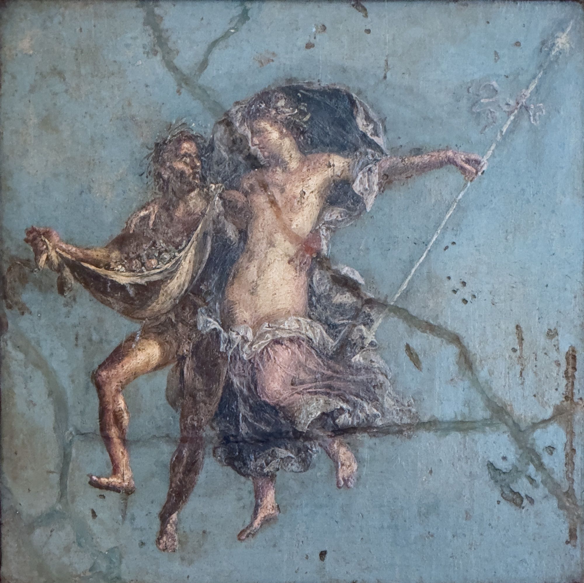 A satyr and maenad float in a blue void, side by side. The satyr has his animal skin garment filled with fruits, and the maenad holds her thyrsus (magic staff) while her pale purple silken garment billows around them.