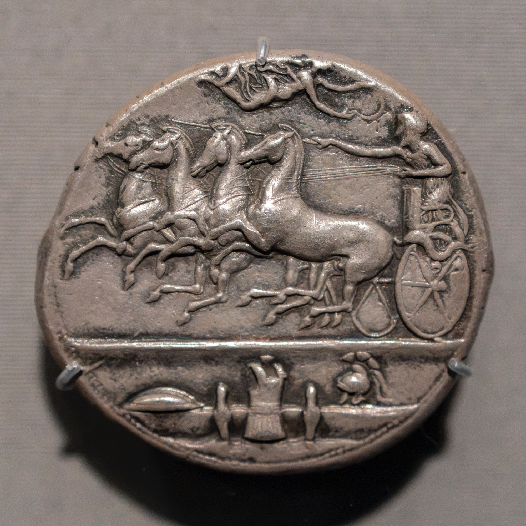 Depicted here on the obverse (front) of this silver coin is a quadriga (four-horse chariot), with Nike flying above and crowned the victorious charioteer. The armor below that scene is described as a 'panoply'. 

There is an inscription - AΘΛΑ ('athla') - the root of 'athletics'. 

Greek, Syracuse, Sicily (part of Magna Graecia, Great Greece, the Greek colonies in Italy), ca. 405-400 BCE. 

Diameter: 38 mm
Weight: 43.15 g

Getty Villa Museum, on loan from the American Numismatic Society (1967.152.534)