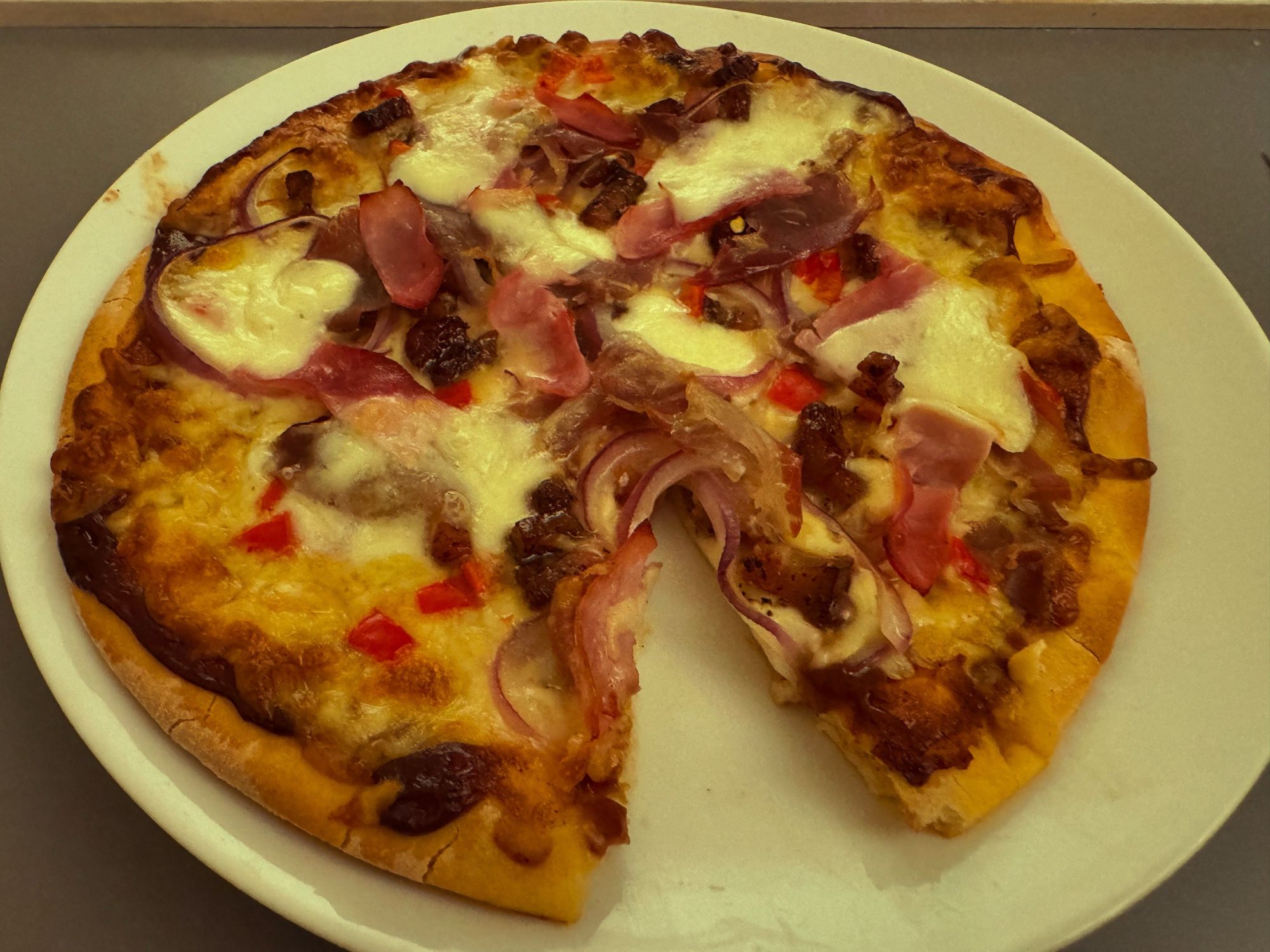 A cooked pizza covered in cheese, pancetta peppers and onion.