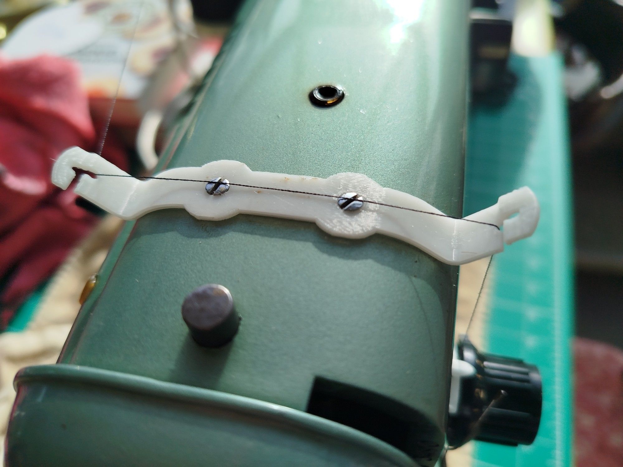 A 3D printed thread holder attached to the top of a green sewing machine.