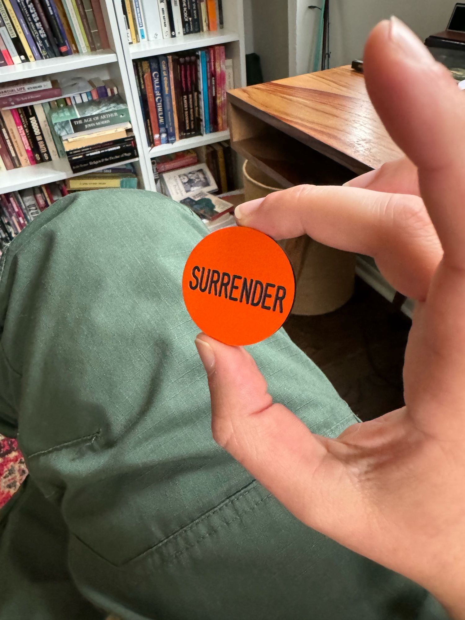 Hand holding an orange plastic button reading SURRENDER