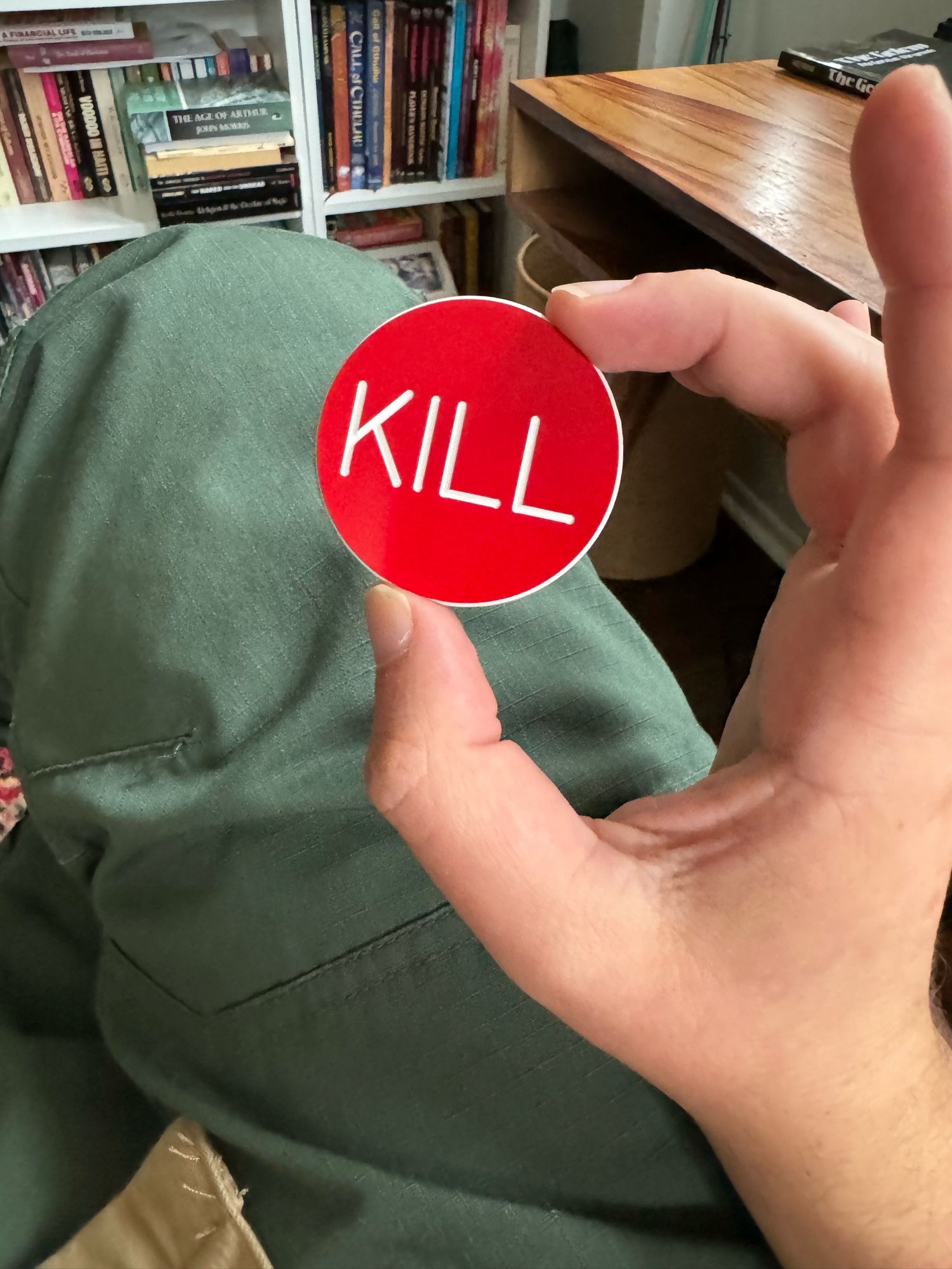 Hand holding a red plastic button reading KILL