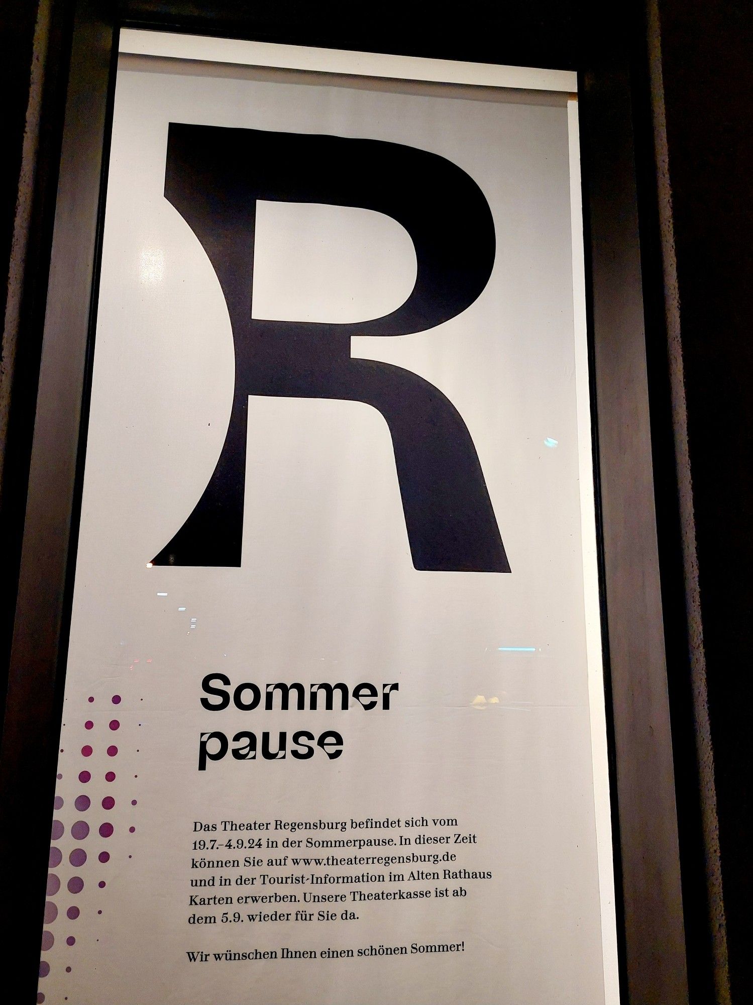 Weißes Febsterbanner mit schwarzer Schrift, beleuchtet. Oben sehr großes R (aus dem Signet Theater Regensburg), darunter: Sommerpause und Info, dass due Theaterkasse ab 5.9. wieder da ist.