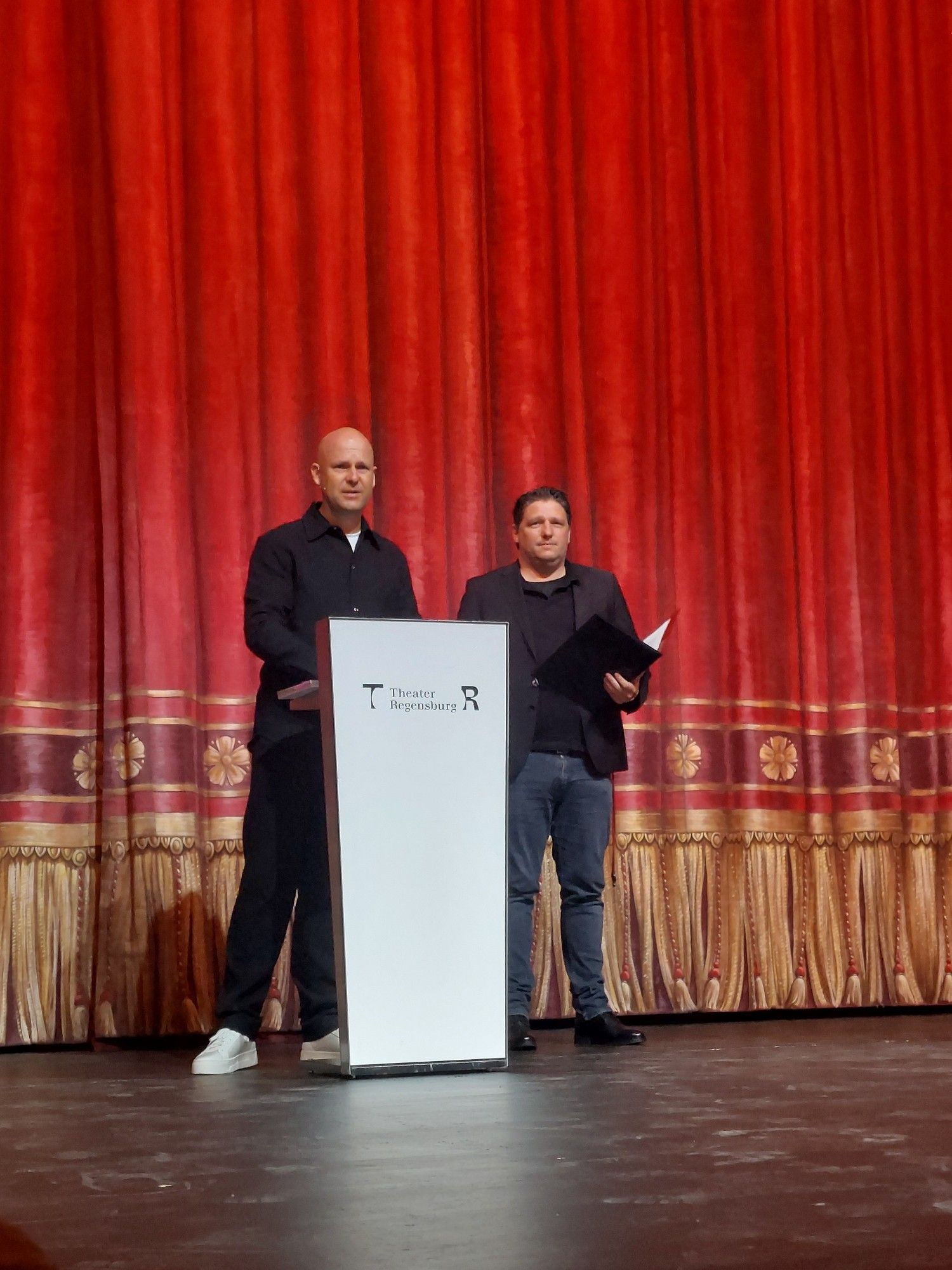 Intendant Sebastian Ritschel und der kaufmännische Direktor Matthias Schloderer vor dem roten Vorhang im Theater am Bismarckplatz.