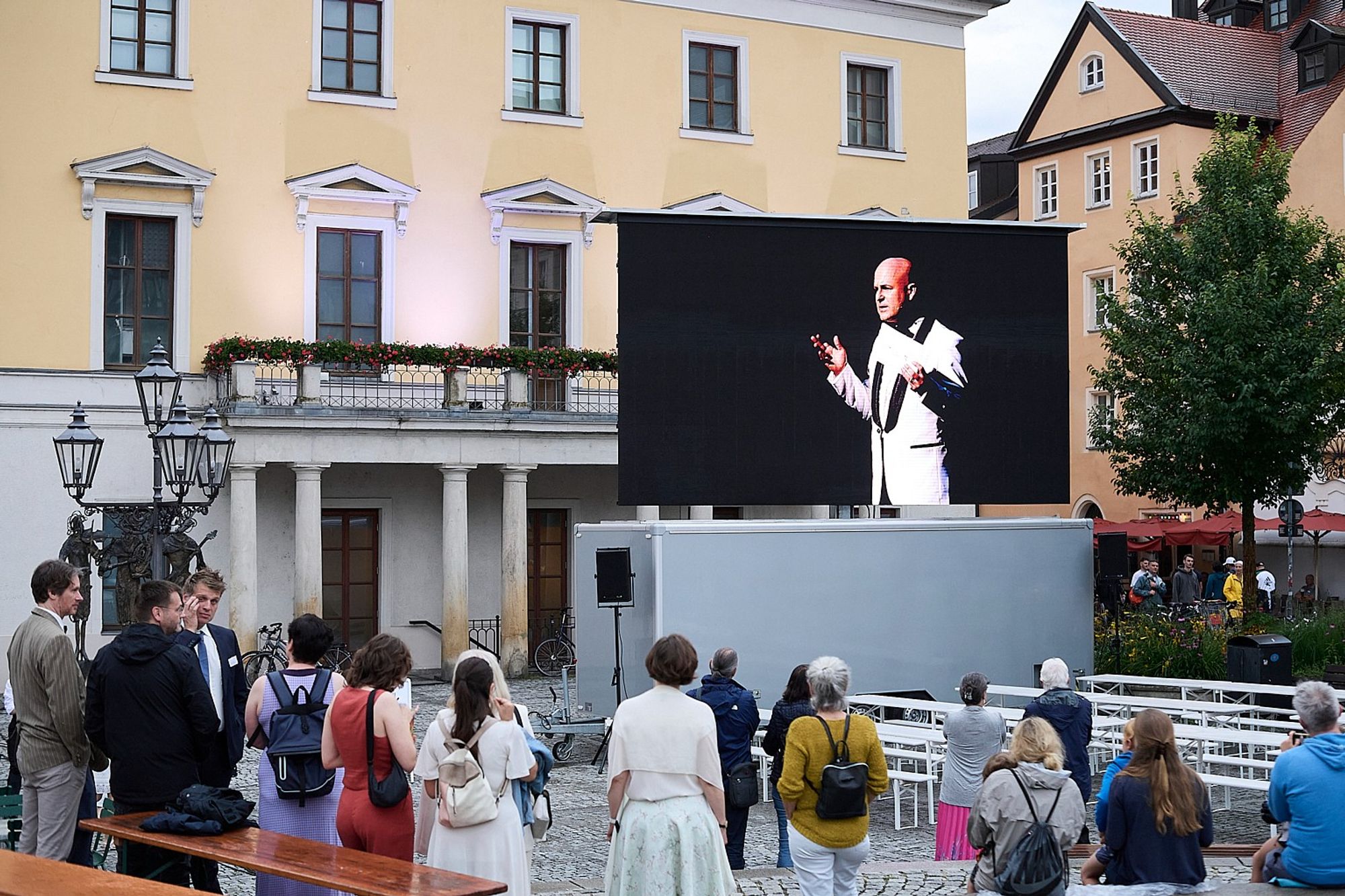 Großleinwand vor dem Theatergebäude bei Tageslicht. Zu sehen ist Intendant Sebastian Ritschel bei seiner Eröffnungsrede zum Sommernachtsball