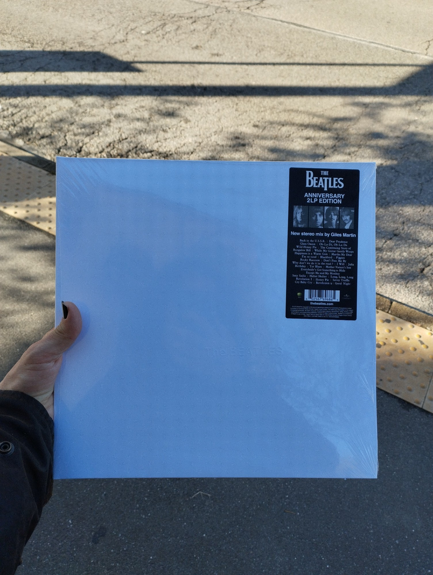 Me holding the anniversary edition of the white album by the beatles. It has a white cover, only interrupted by a label attached to the cellophane packaging. The actual album is fully white.