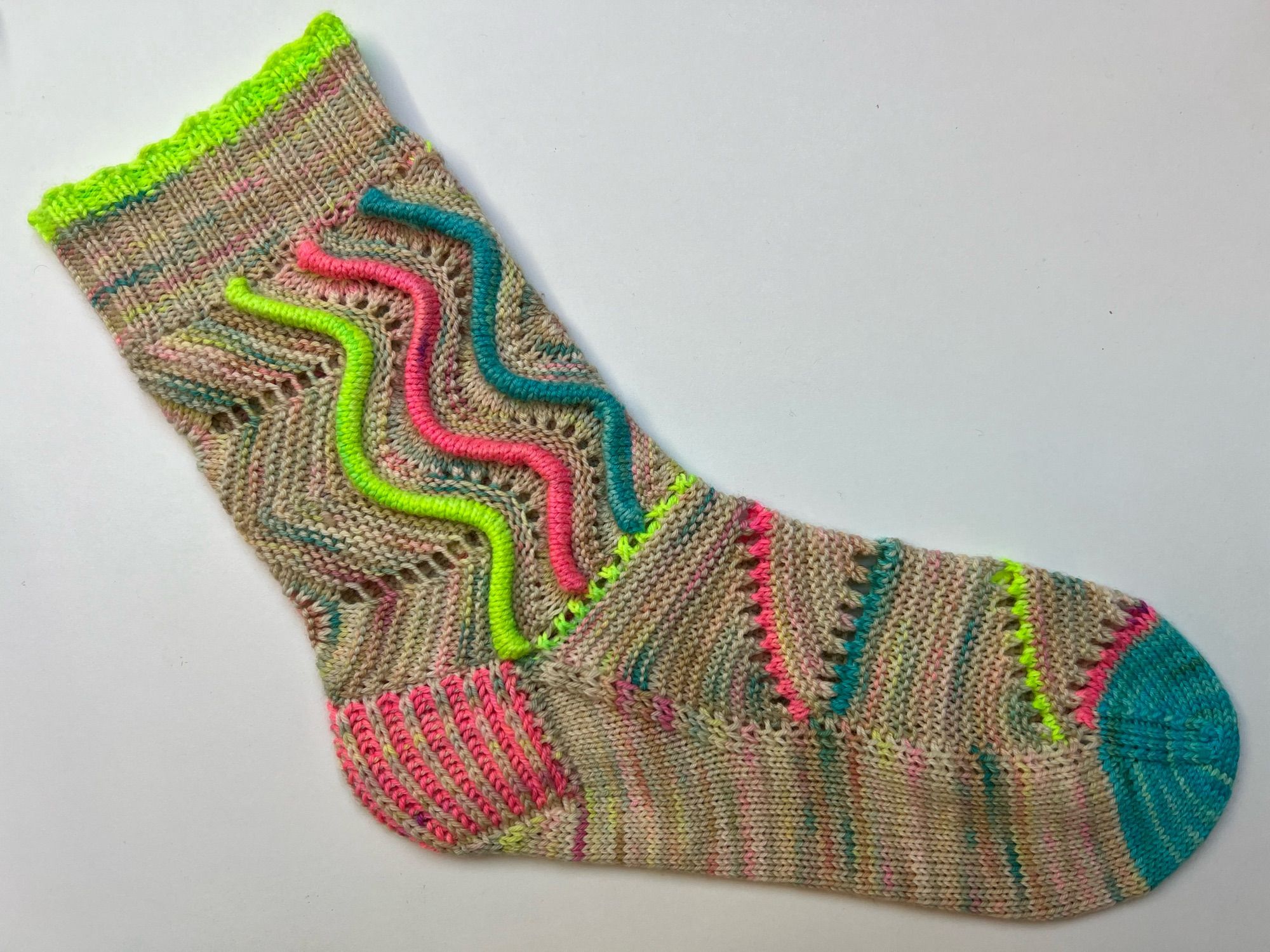 Colourful and textured handknitted sock in a pink, blue and green speckled cream yarn with neon pink, green and blue accents , laid out on a white background.