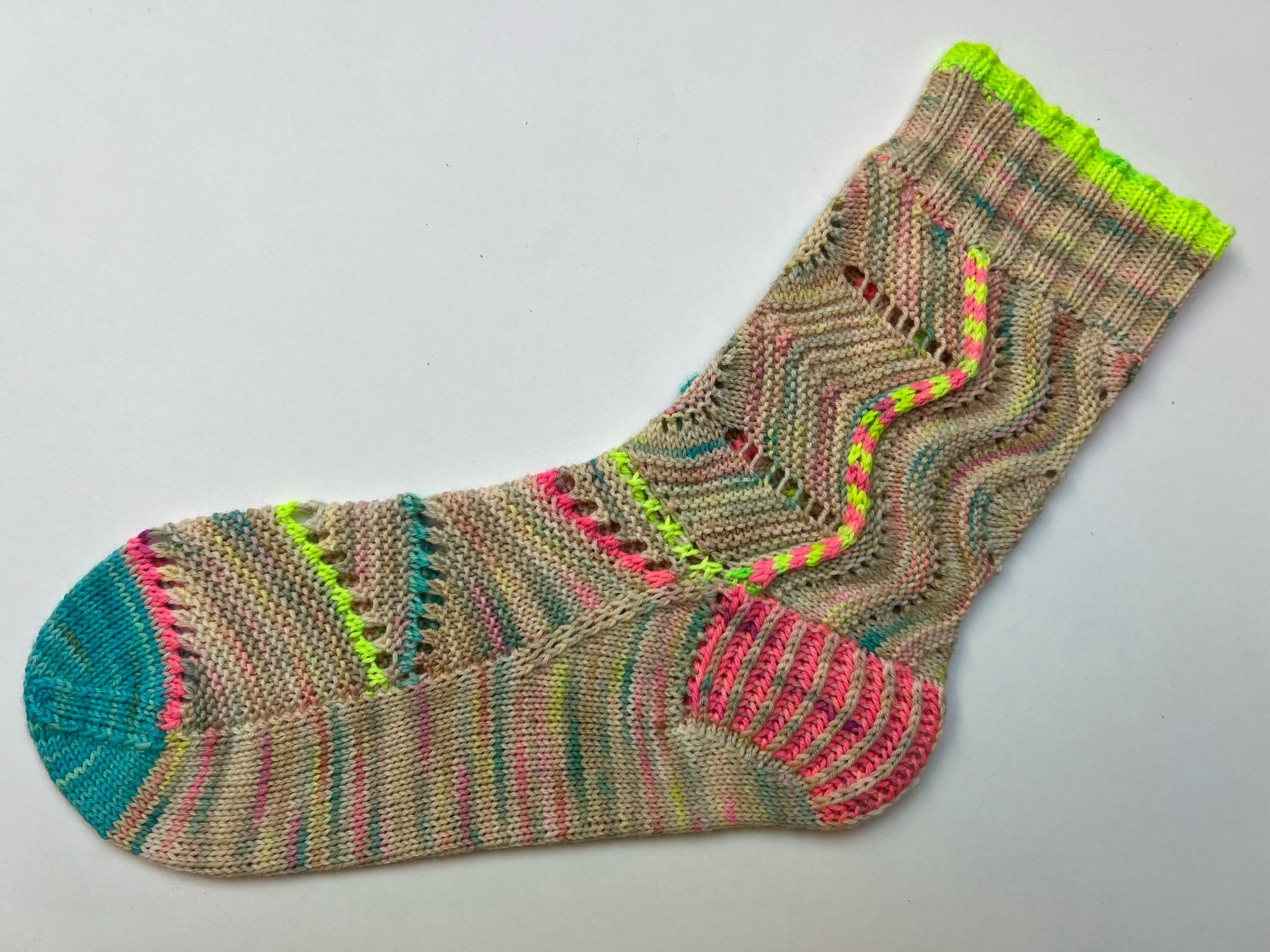 Colourful and textured handknitted sock in a pink, blue and green speckled cream yarn with neon pink, green and blue accents , laid out on a white background.