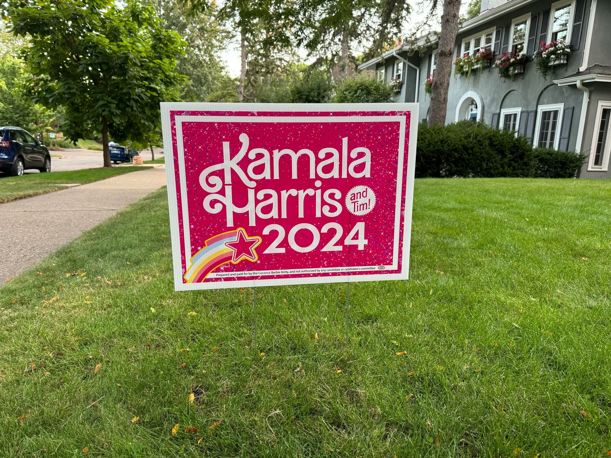 A Barbie themed Harris sign in pink with white writing in the Barbie font. It says Kamala Harris 2024 with a small star that says And Tim!