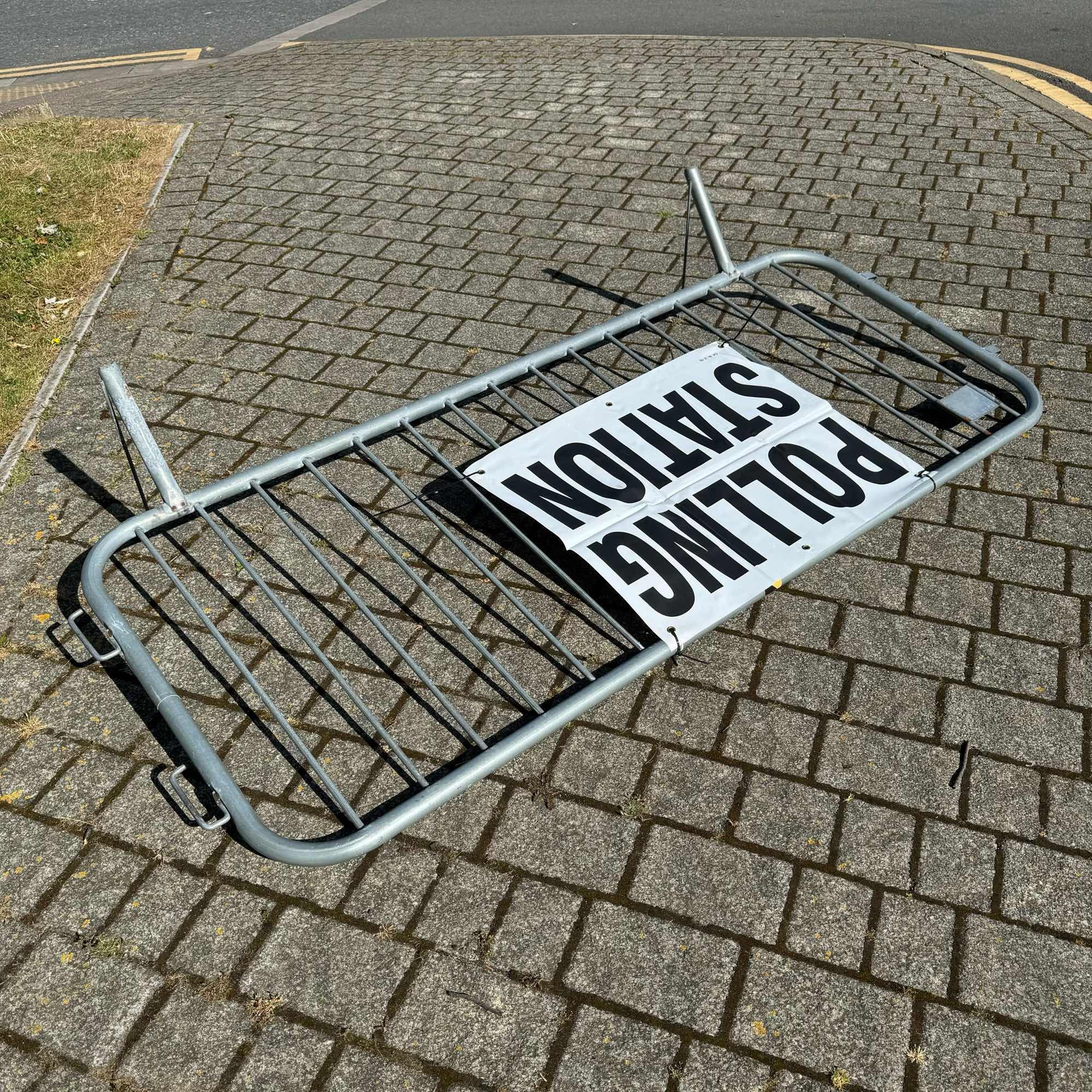 A polling station sign attached to a section of temporary fence which has fallen down in the wind.